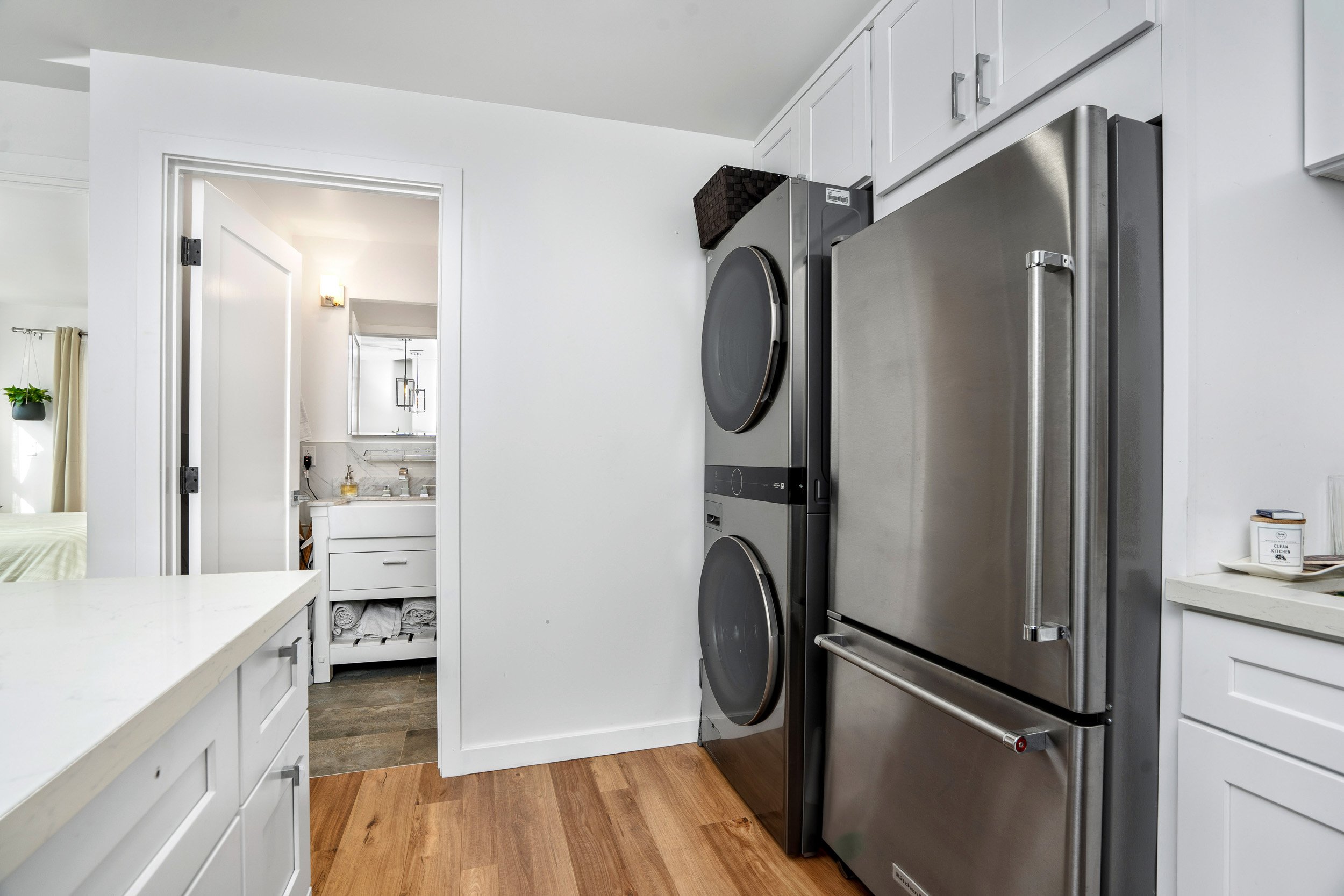 Modern laundry room with white cabinets, a stainless steel refrigerator, washer and dryer, and wood flooring.