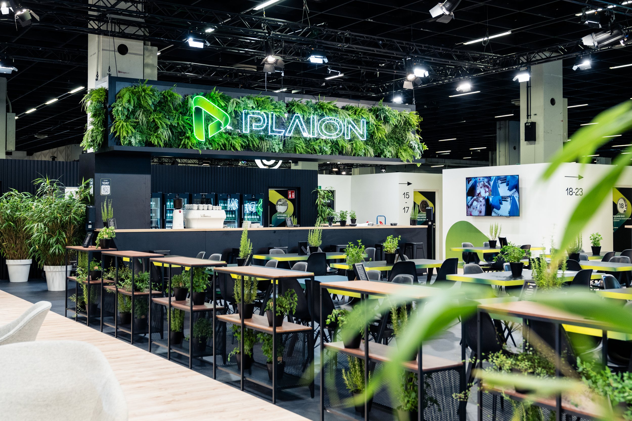 Indoor event space with green plants and modern decor, including a neon sign that says 'PLAION.'