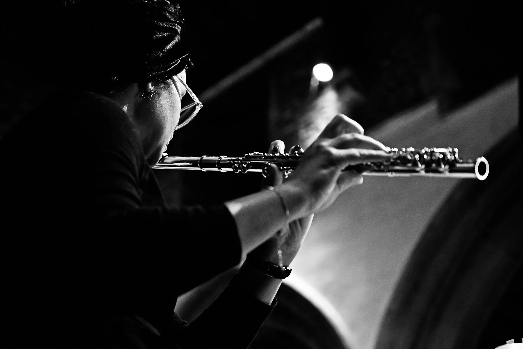 A person playing the flute in a dimly lit environment, seen from the side with focus on the hands and flute.