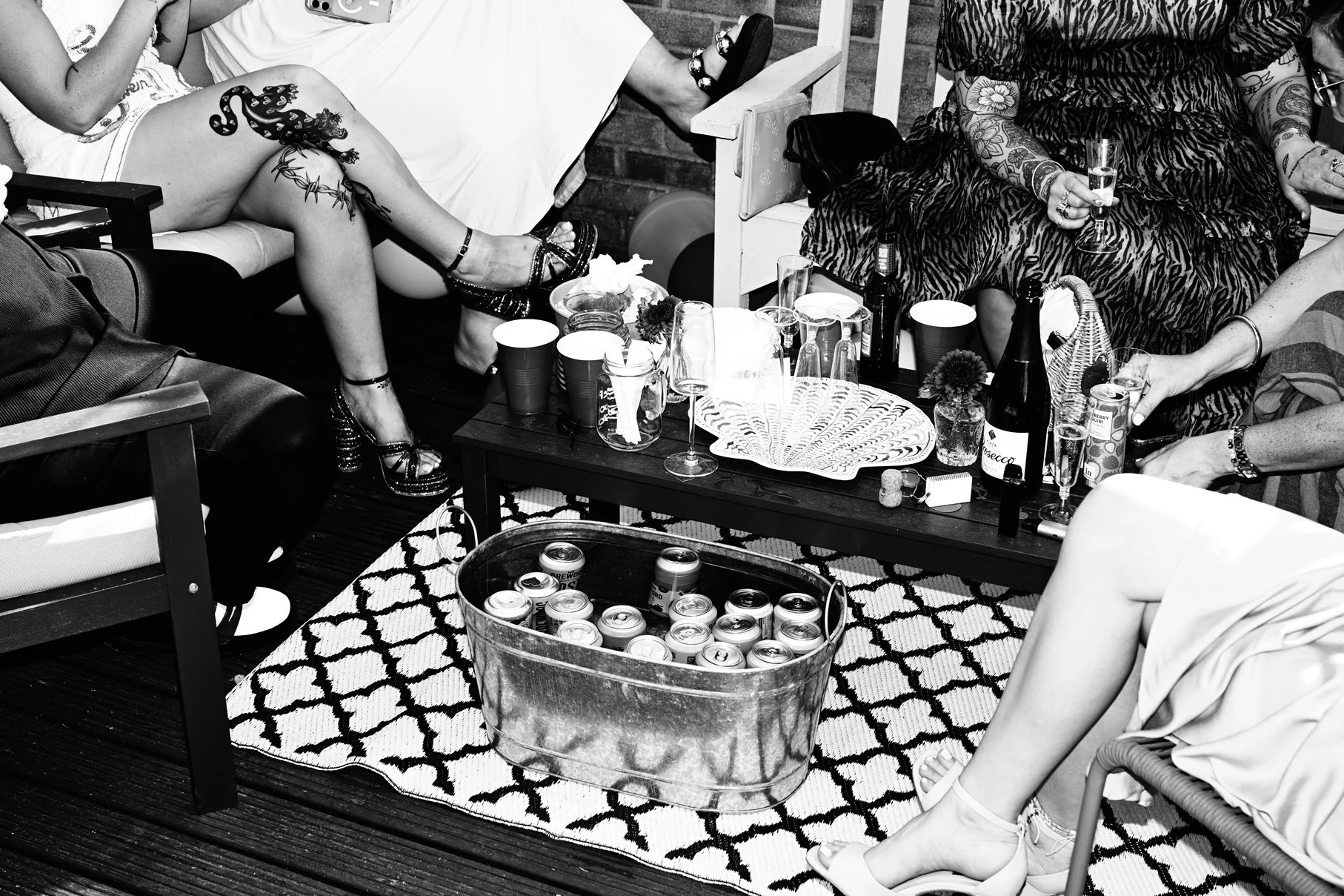 Group of women sitting around a table at a party, with drinks, snacks, and decorative items on the table, with their legs crossed and wearing stylish clothing.