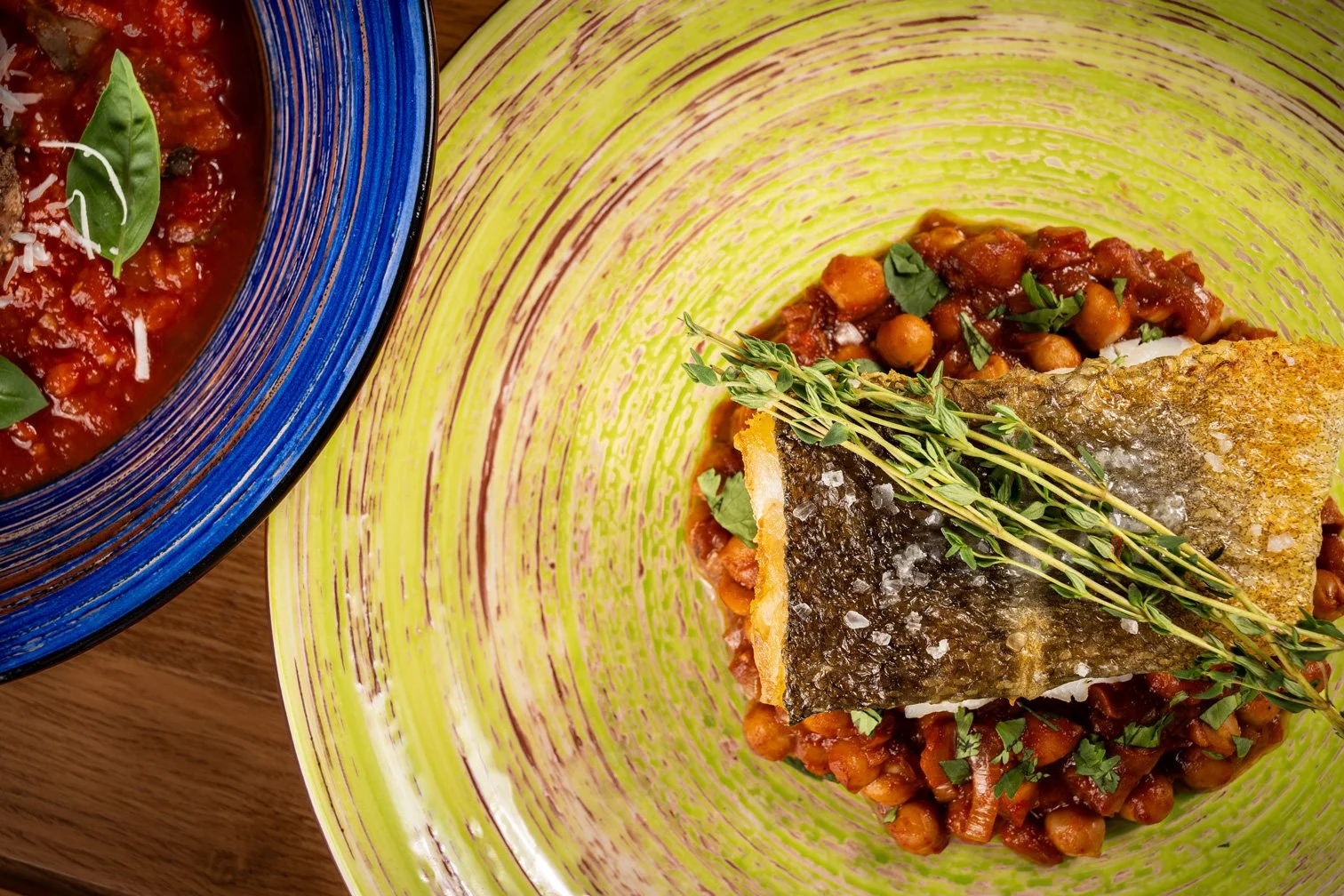 A plated dish with a crispy cod fish fillet on chickpeas, garnished with herbs, and a bowl of tomato sauce with basil on the side.