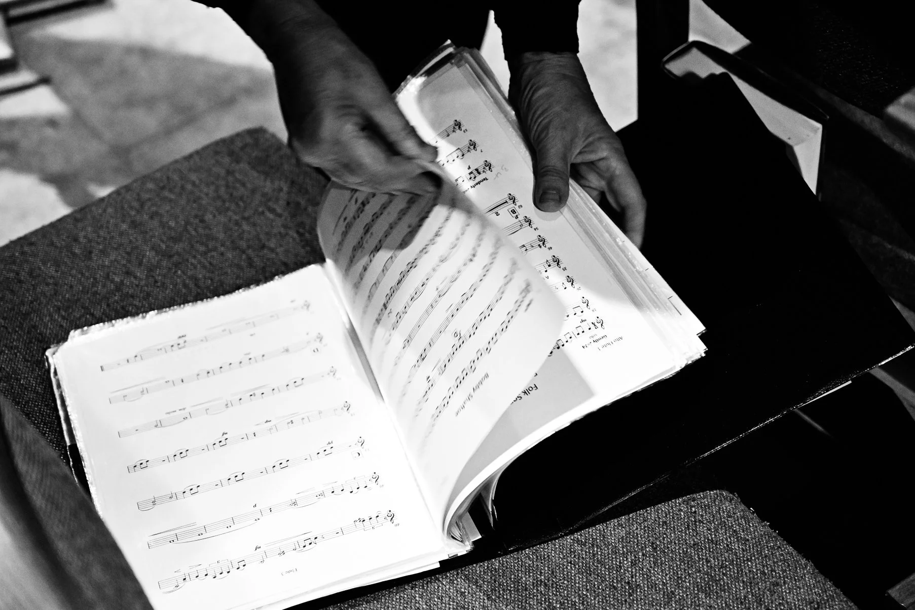 Close-up of a person flipping pages of a sheet music book on a piano bench, in black and white.
