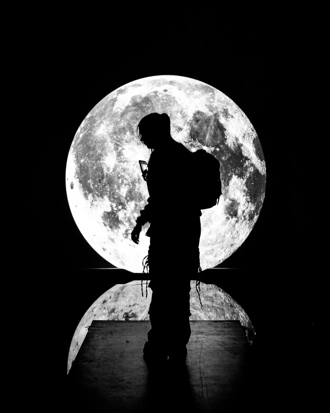 Silhouette of a person with a backpack looking at a smartphone in front of a large illuminated moon.