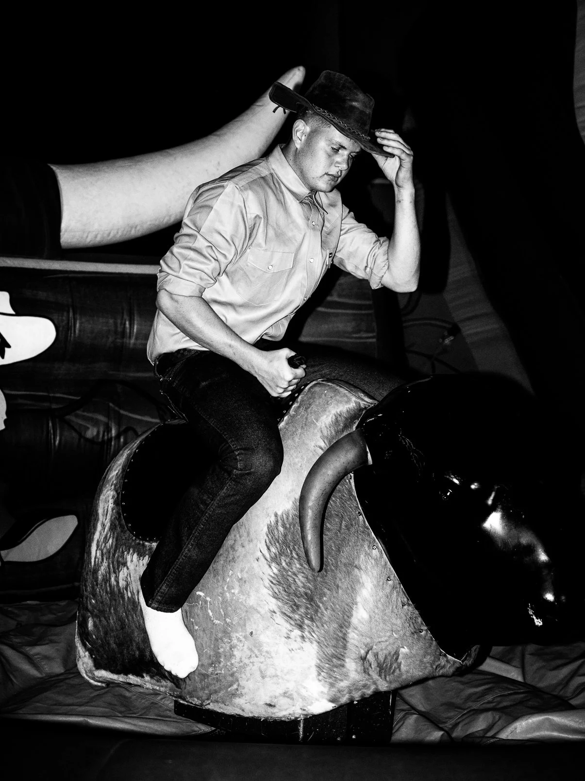 A person wearing a hat and casual clothing riding a mechanical bull.