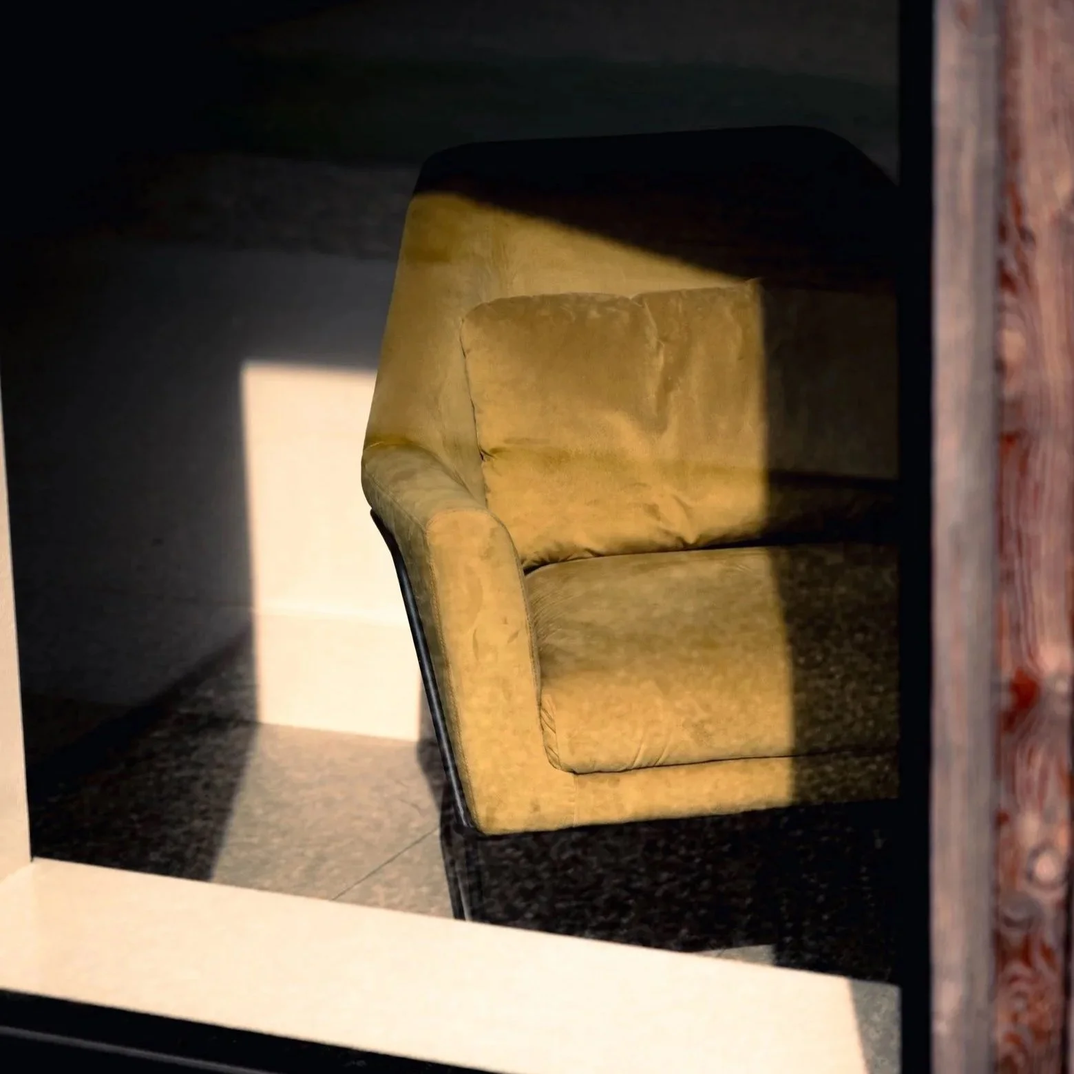 Yellow upholstered armchair with dark metal legs in a room with black stone flooring, partially shown through a mirror.