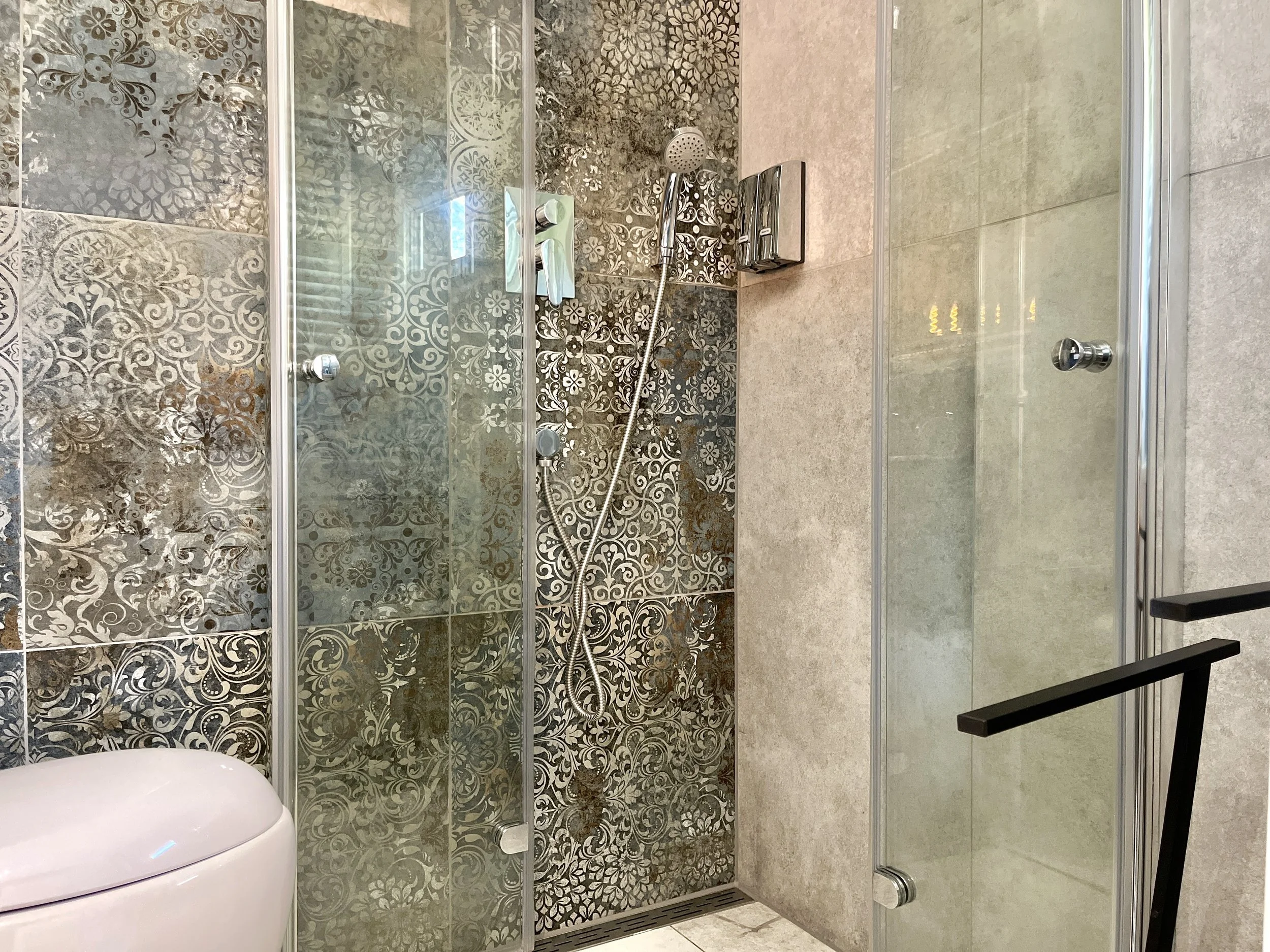 A bathroom shower area with patterned tiles, a glass door, and a handheld showerhead.