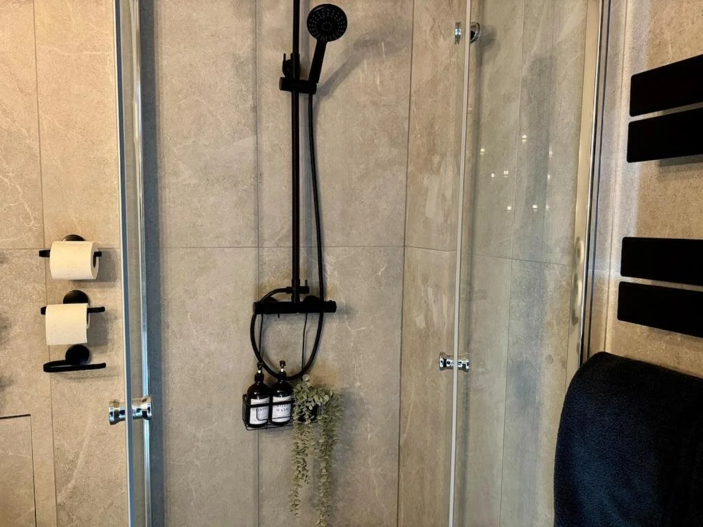 A modern bathroom shower with black fixtures, a glass door, and beige tiled walls.