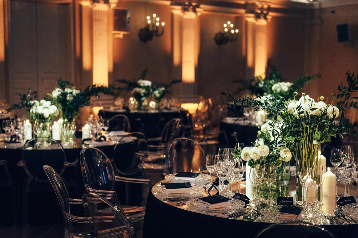 Elegant banquet table setup with floral centerpieces, candles, and glassware in a dimly lit, ornate room.