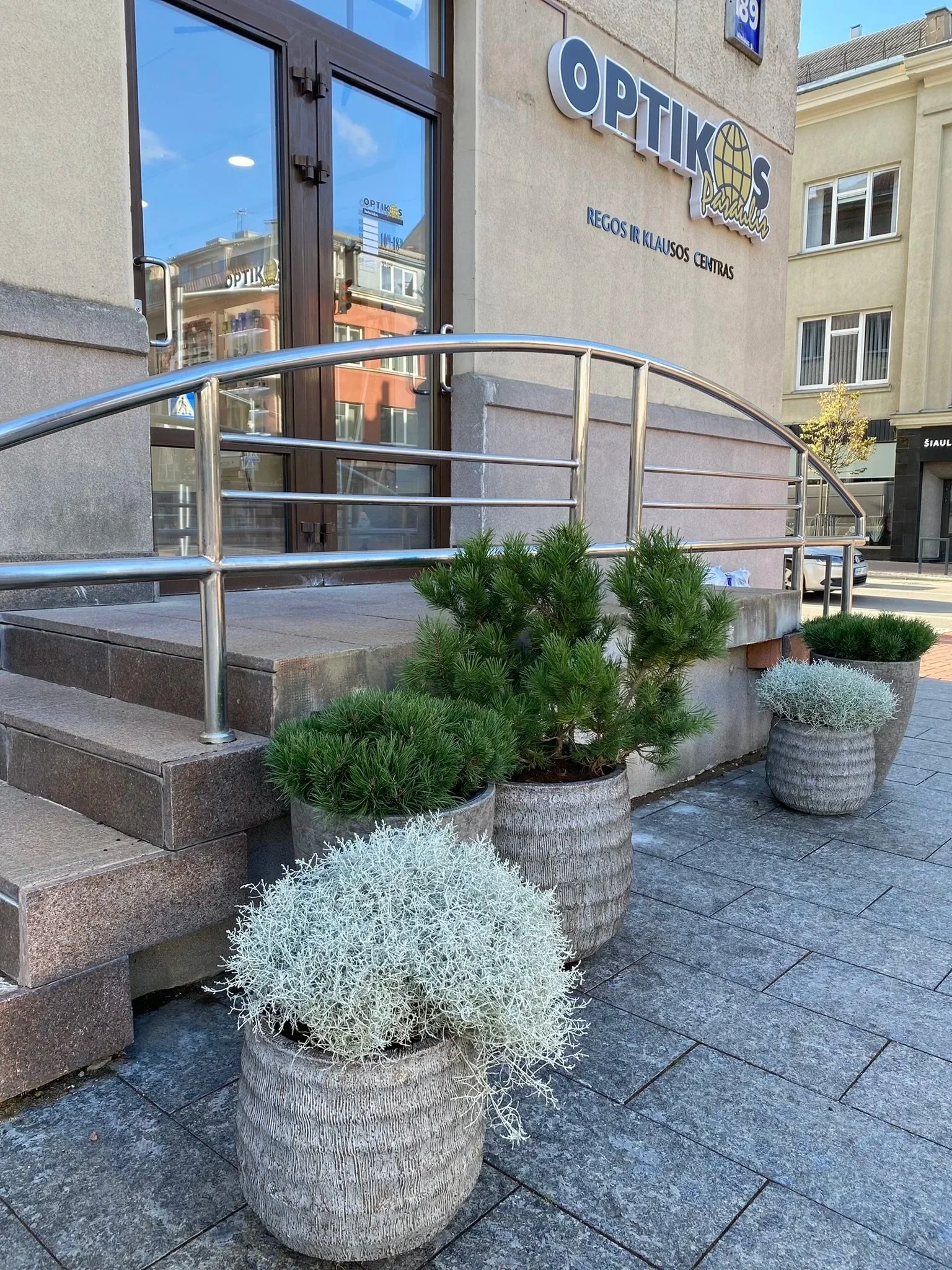 Outside of an optometry clinic with potted plants and a stairway leading to the entrance.