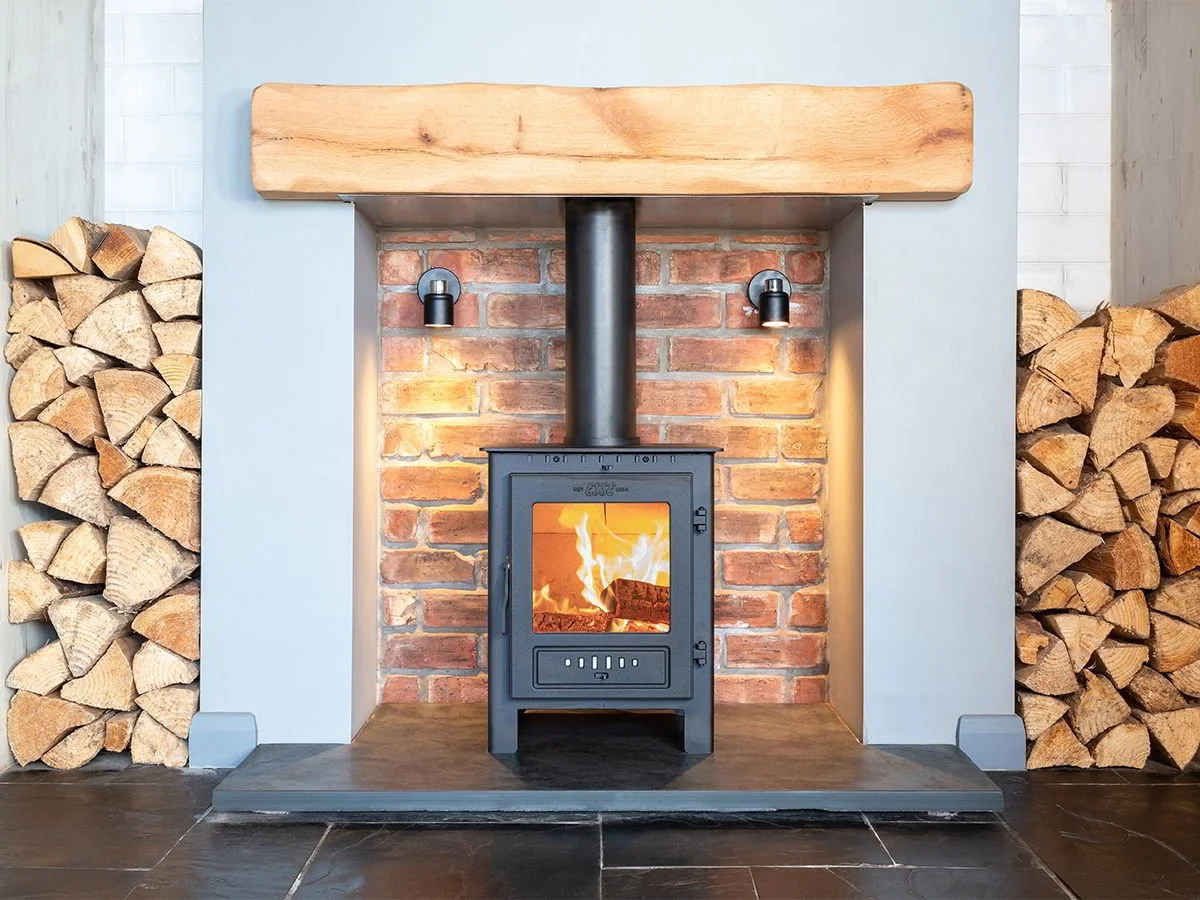 A fireplace with a wood stove, brick background, and wood logs stacked on both sides.