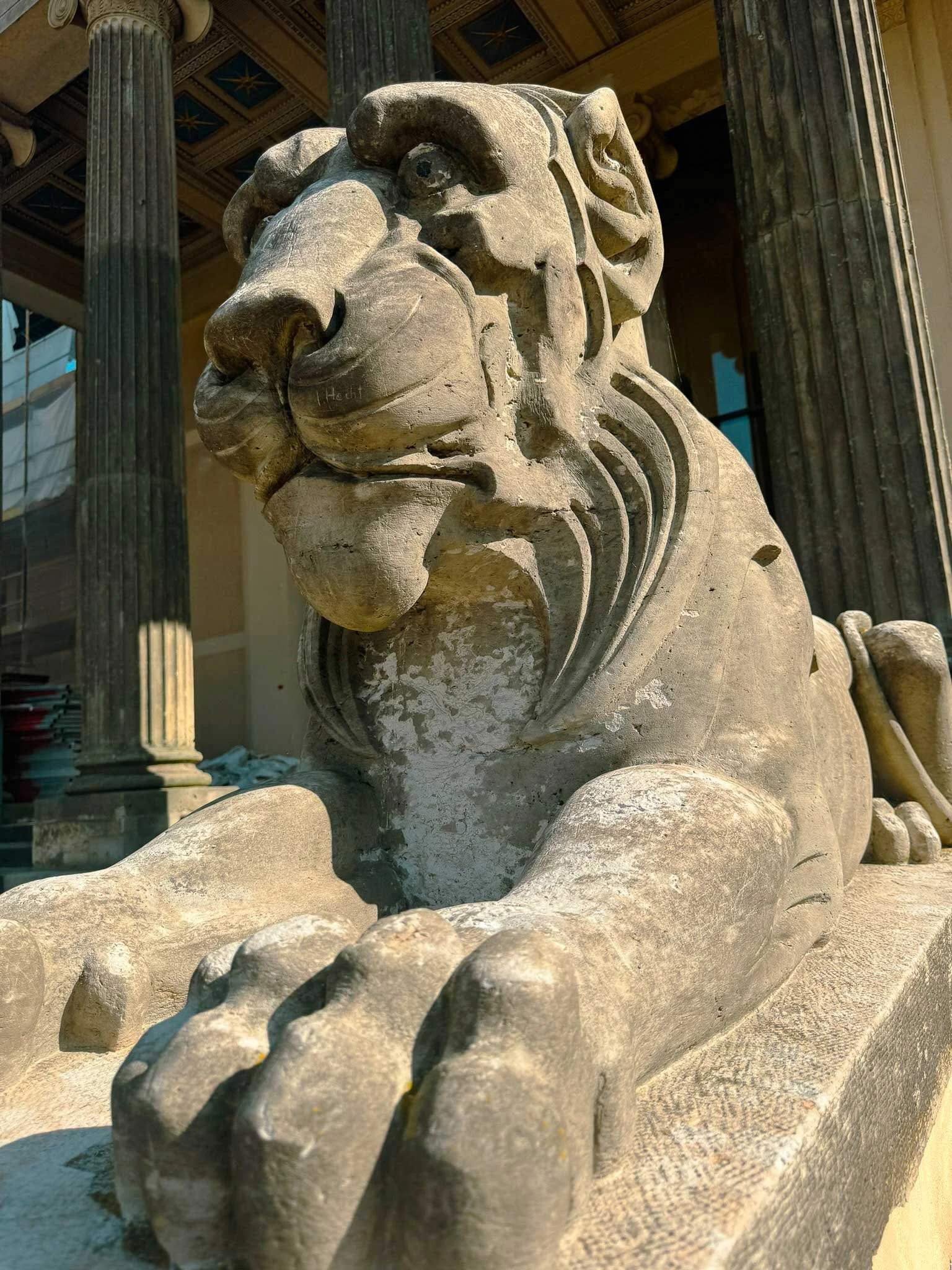 Steinerne Statue eines Löwen vor einem historischen Gebäude mit Säulen und verzierten Decken.