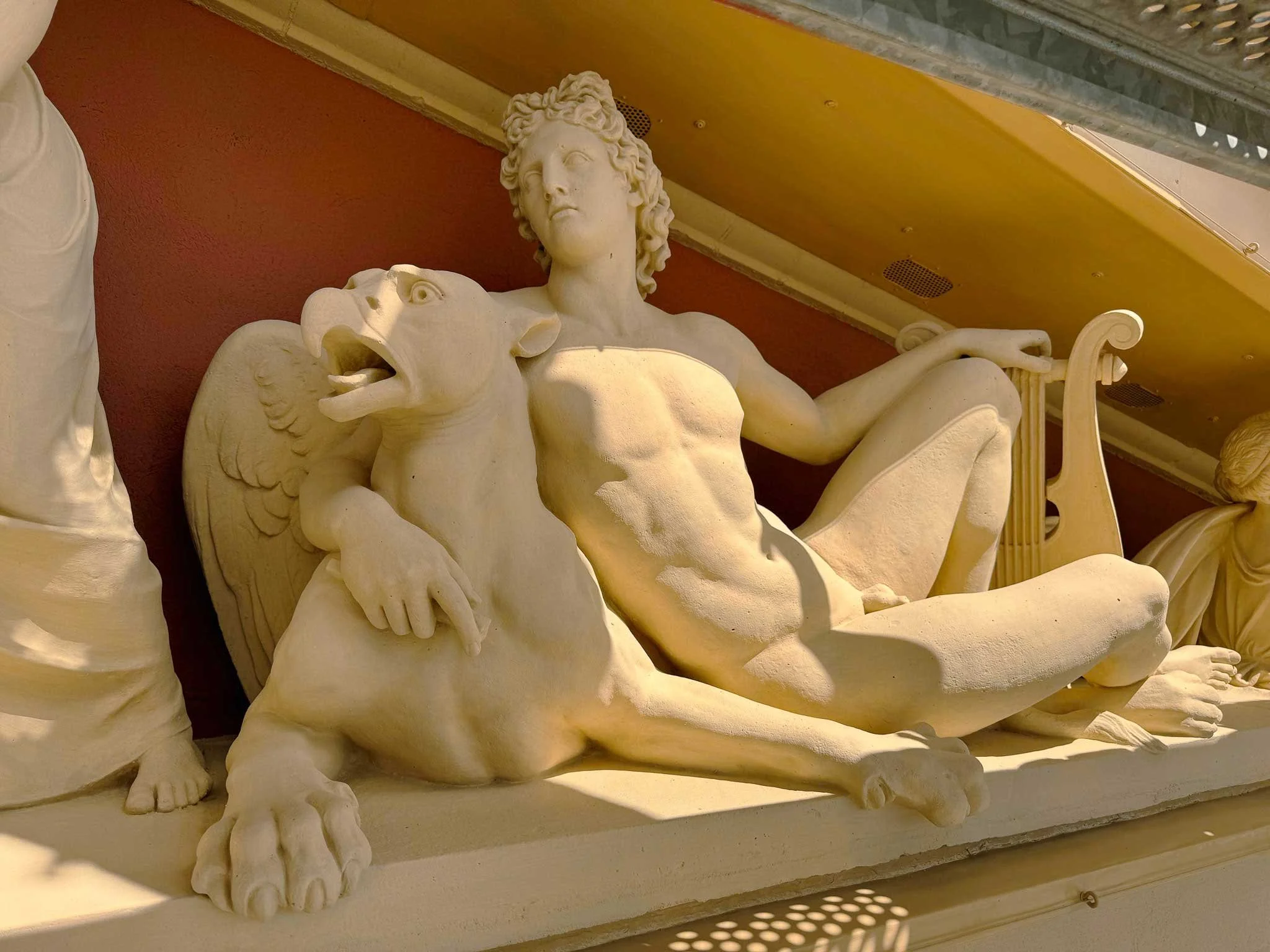 Bild einer weißen Skulptur, die einen mythologischen oder historischen Charakter darstellt, mit lange, lockige Haare, die zu den Schultern fallen, und einer Pose, die einen Löwen umfasst.