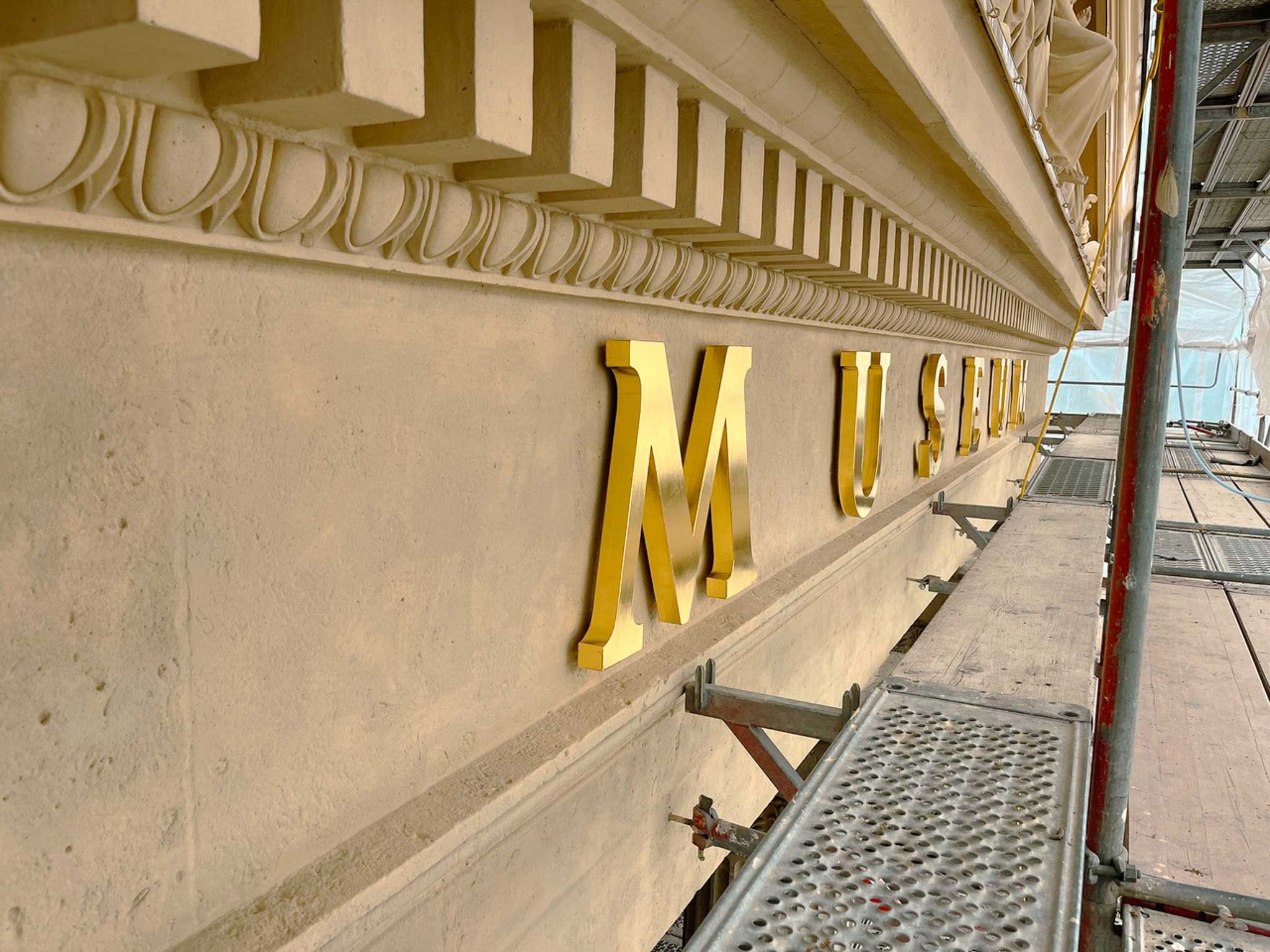 Baugerüst vor einer Hausfassade mit gelben Buchstaben, die teilweise sichtbar sind.