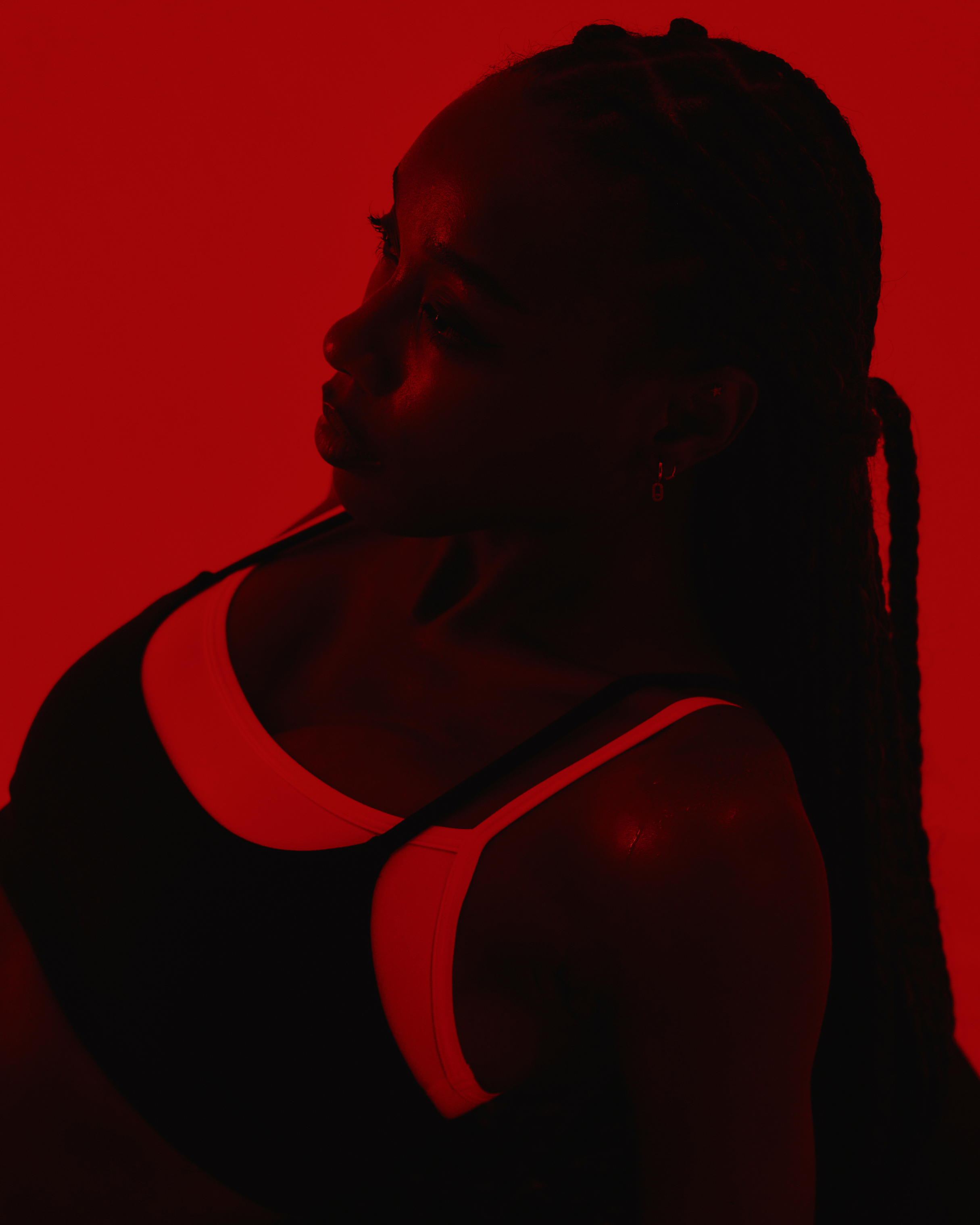 Silhouette of a woman with braided hair against a red background, wearing a sports top.