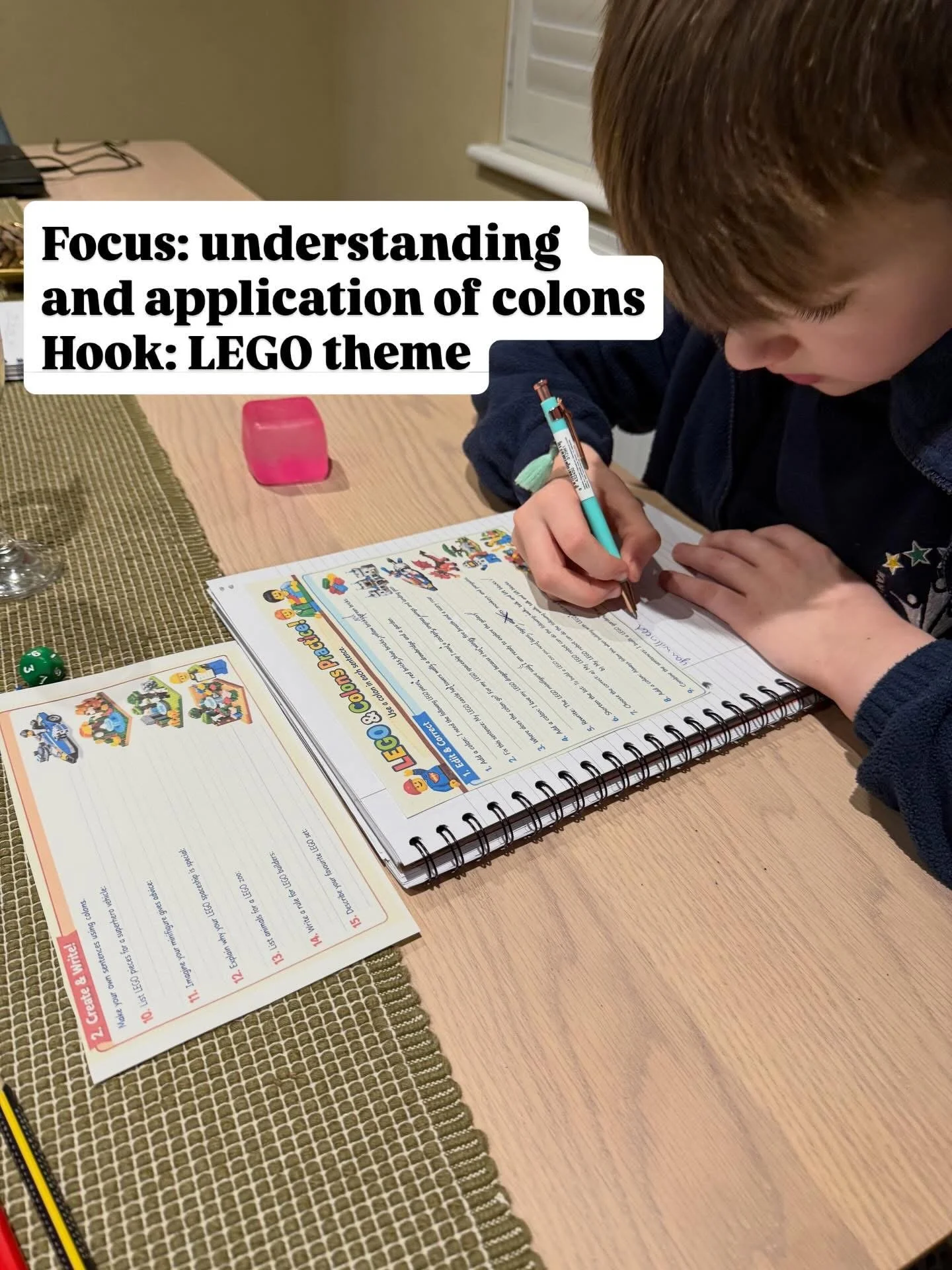 A young boy is writing in a notebook at a wooden table, with educational materials related to LEGO on the page.