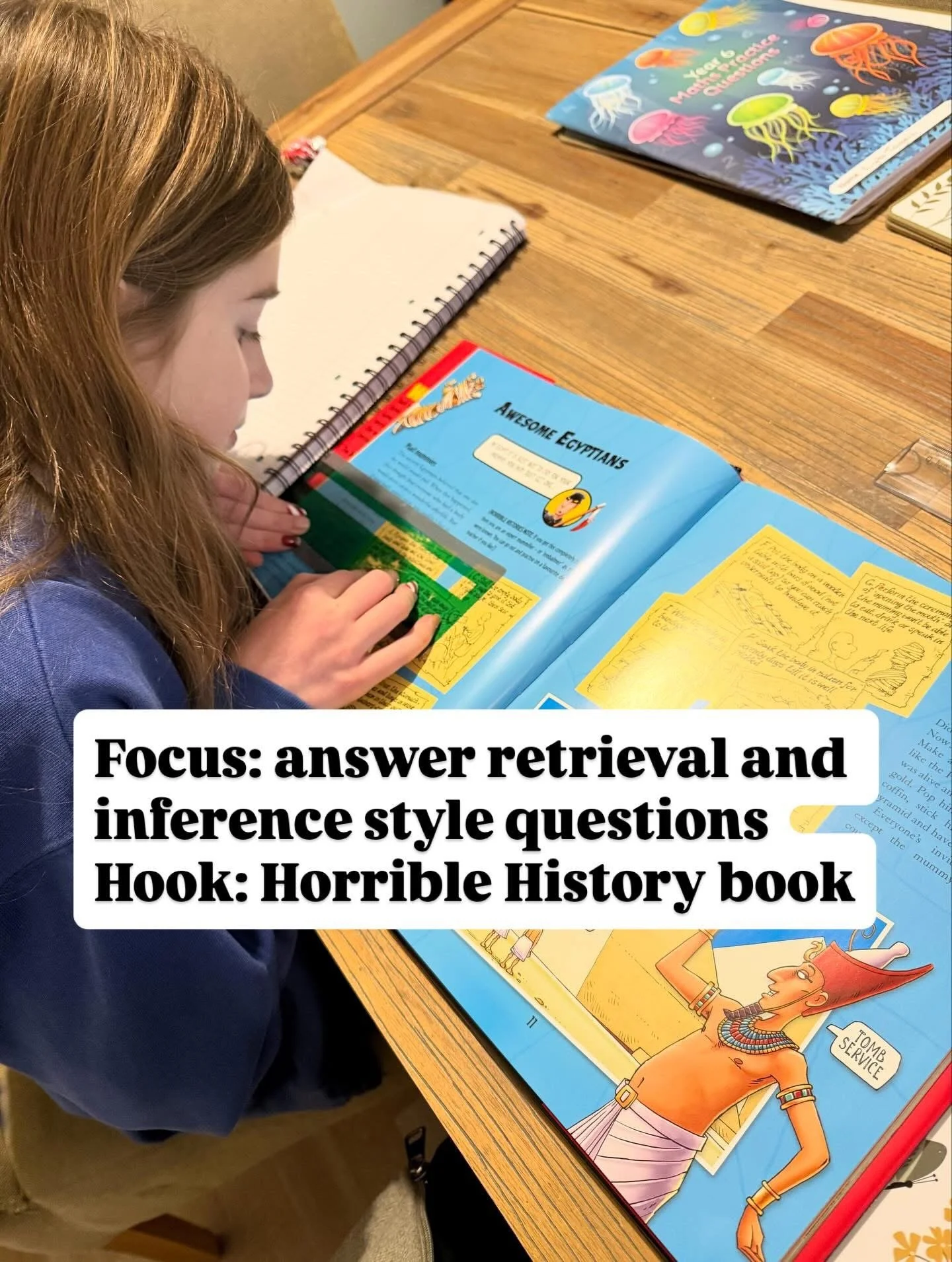 A girl studying a colorful history book titled 'Horrible Histories' at a wooden table, with other books visible nearby, including one with an underwater scene of jellyfish.