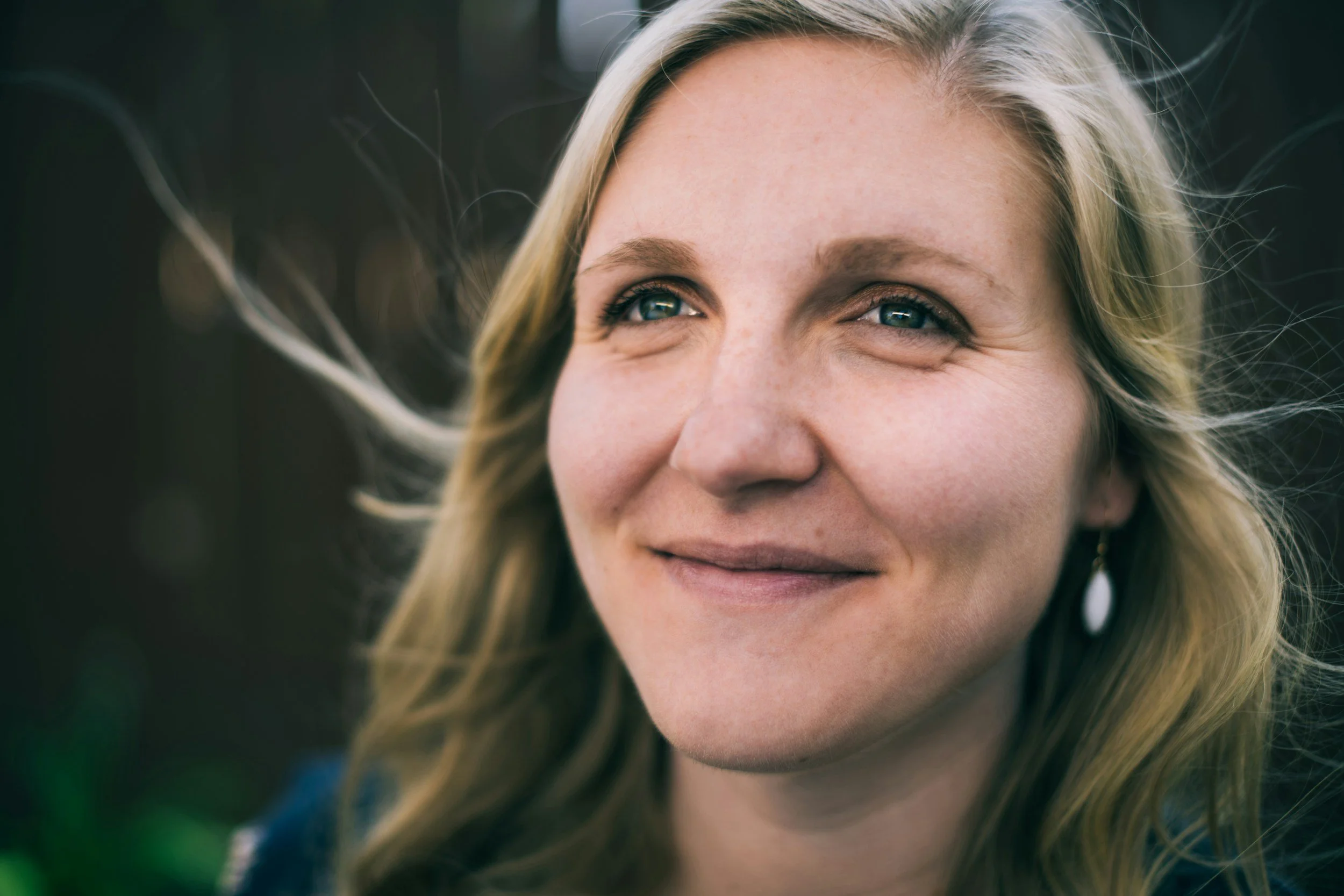 Close-up of a smiling woman with blond hair and blue eyes, outdoors.