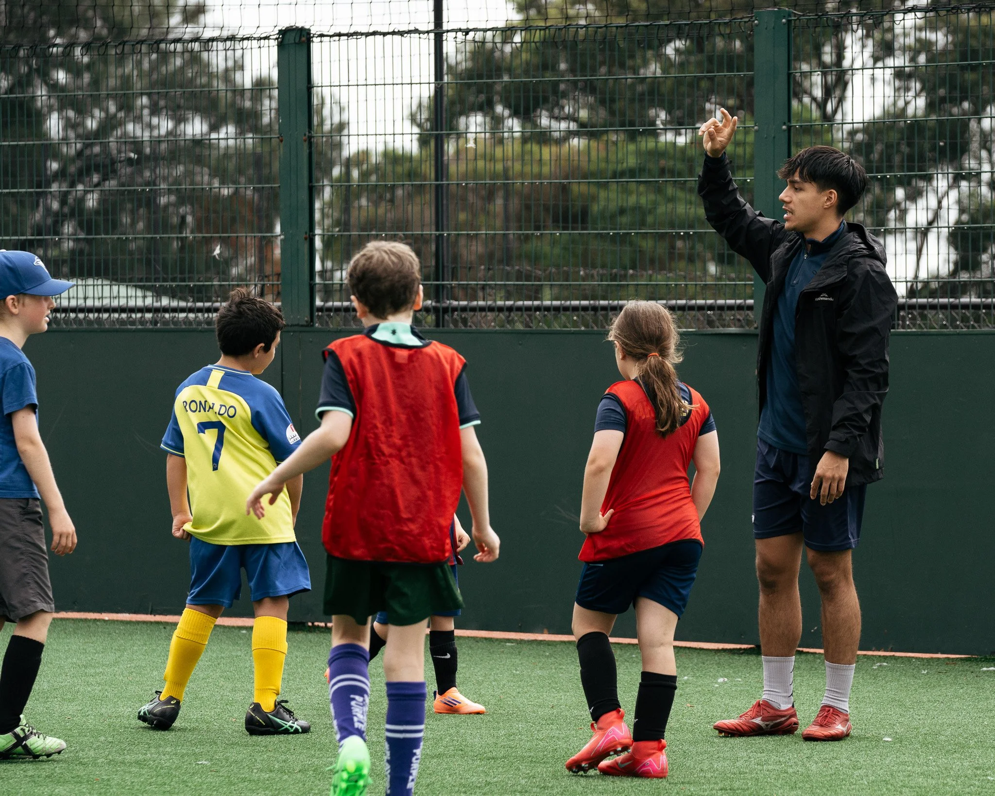 Football coach giving instructions to young players during a small-group training session.