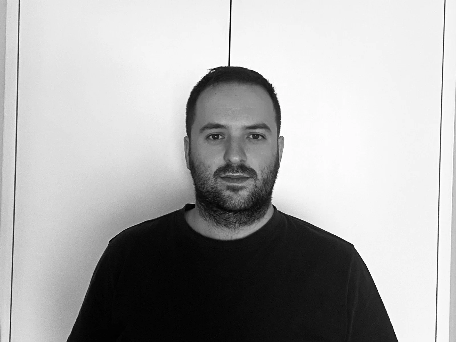 Retrato en blanco y negro de un hombre con barba con fondo de paredes blancas.