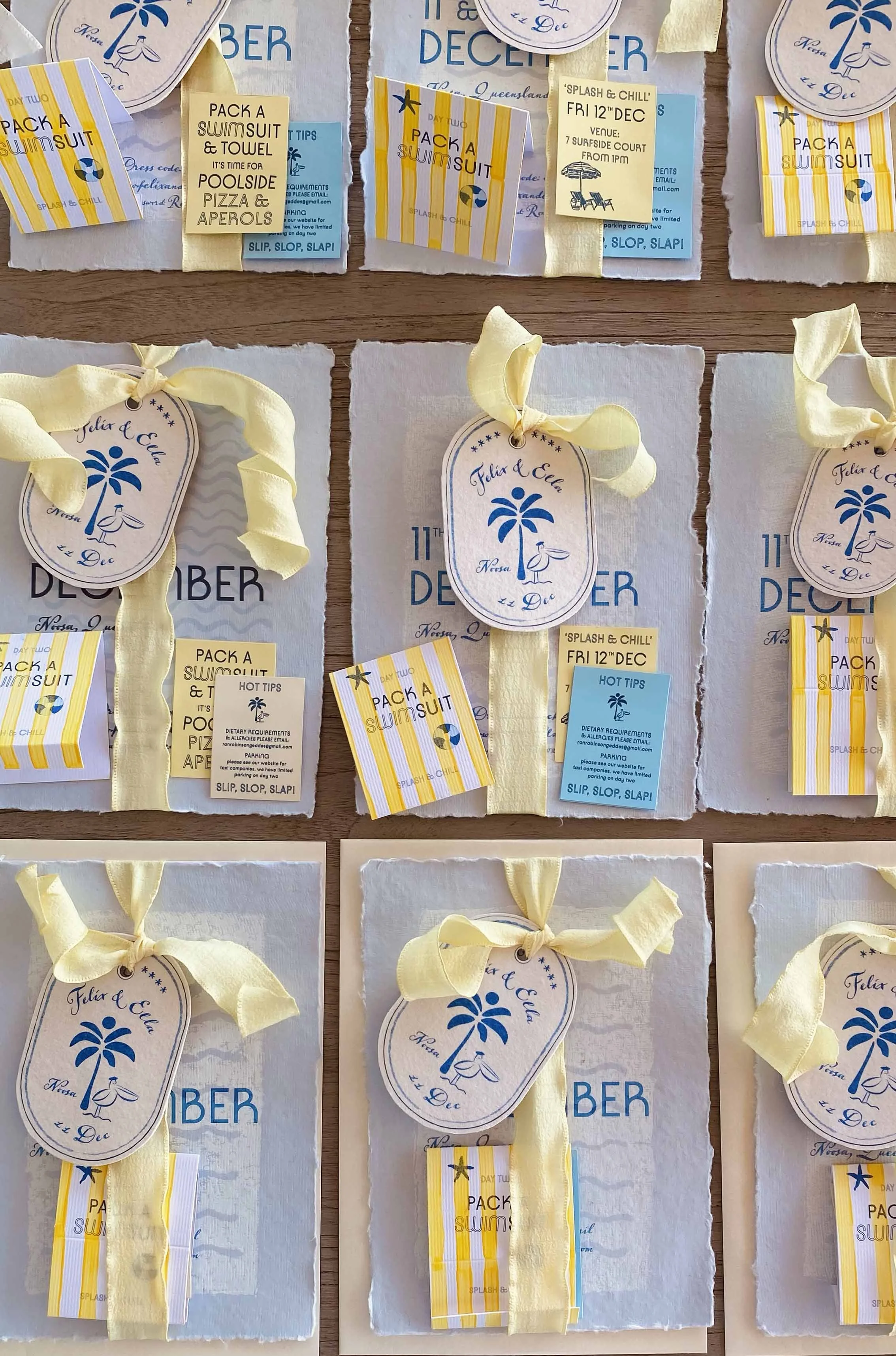 Collection of white paper envelopes with yellow ribbons, each featuring a beach-themed tag with a blue palm tree and a seagull, and some with event details for a holiday party in December.