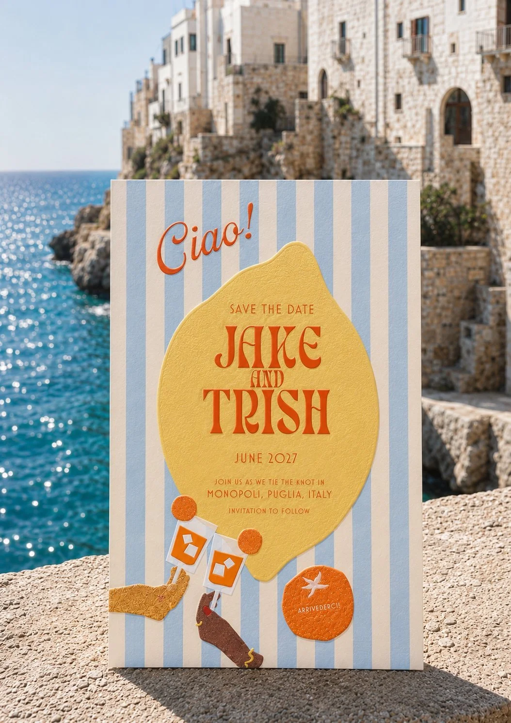 Save the date card with a lemon design for a wedding in June 2027, featuring the names Jane and Trish, set against a coastal backdrop with buildings and water.