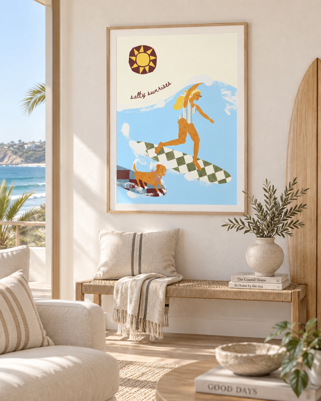 Decorative beach-themed poster with a woman surfing on a wave and a dog on a surfboard, titled 'salty sunrises', hanging on a wall in a bright living room with coastal decor.