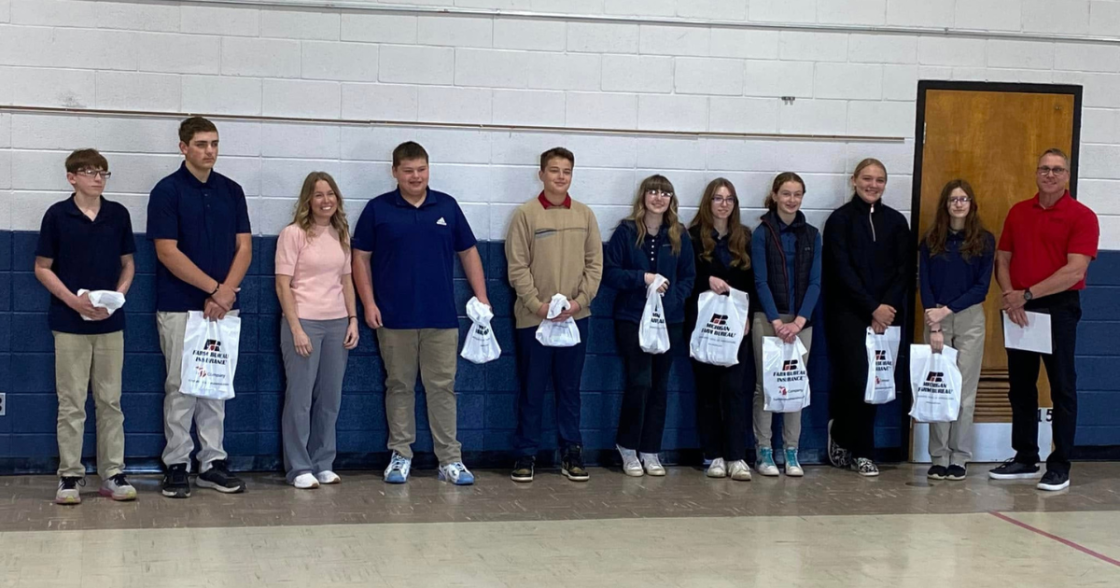 School group of students and teacher standing in a line in a gymnasium holding awards and gift bags.