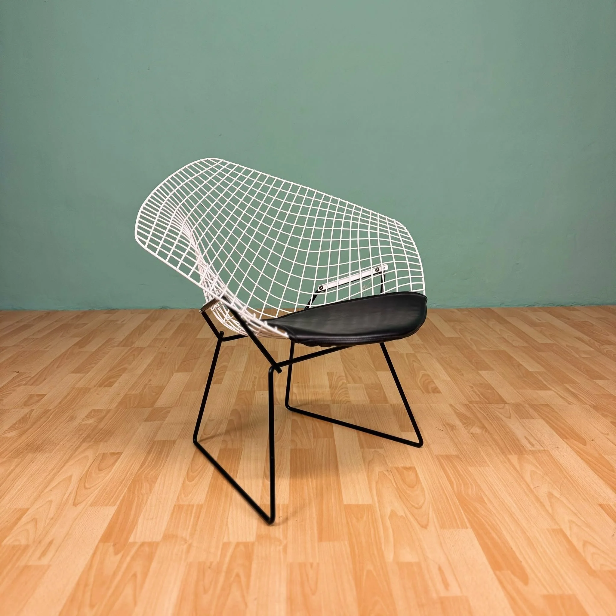 White wire chair with black cushion on wooden floor against light green wall, Aymerick Rondeau Furniture Emporium Alhaurin second hand furniture shop