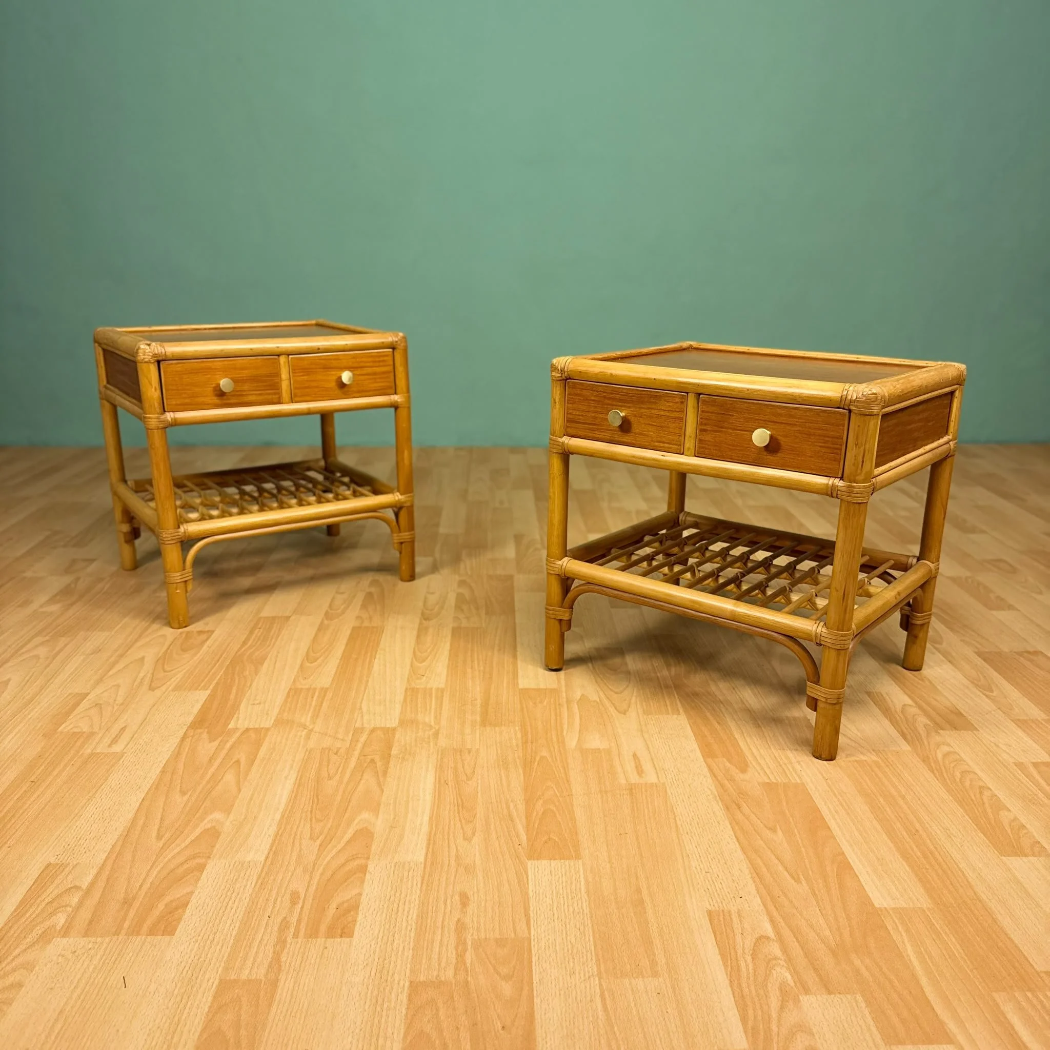 Two rattan bedside tables with drawer handles, placed on a wooden floor against a plain turquoise wall. Aymerick Rondeau Furniture Emporium Alhaurin second hand furniture shop