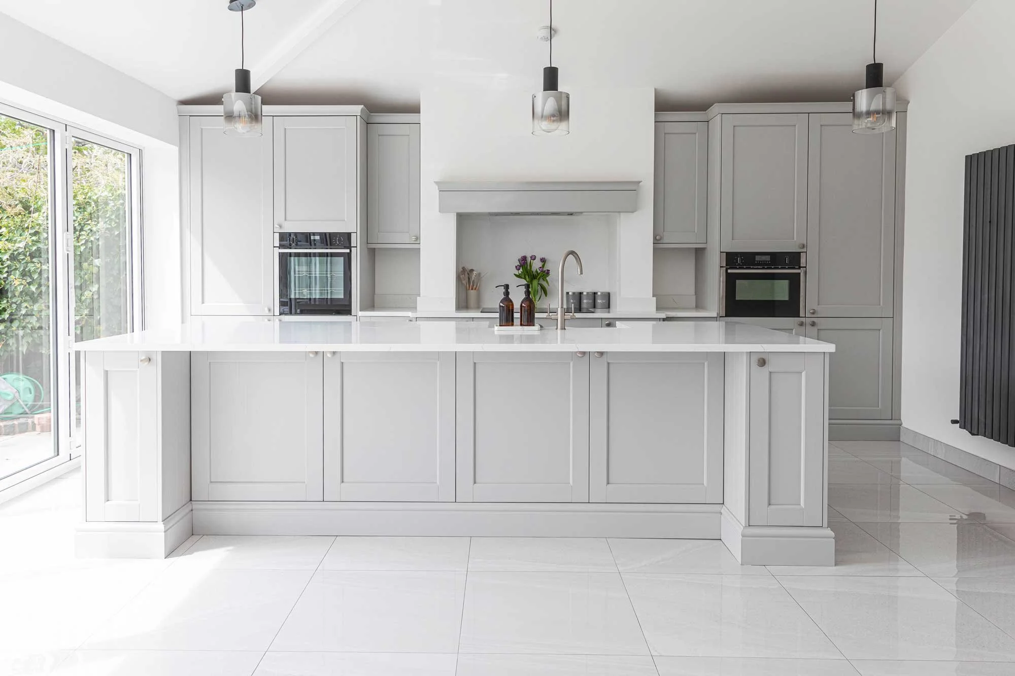 Close-up of a modern white kitchen island with a marble-effect quartz worktop, a chrome spring-neck tap, and a pop-up electrical socket.