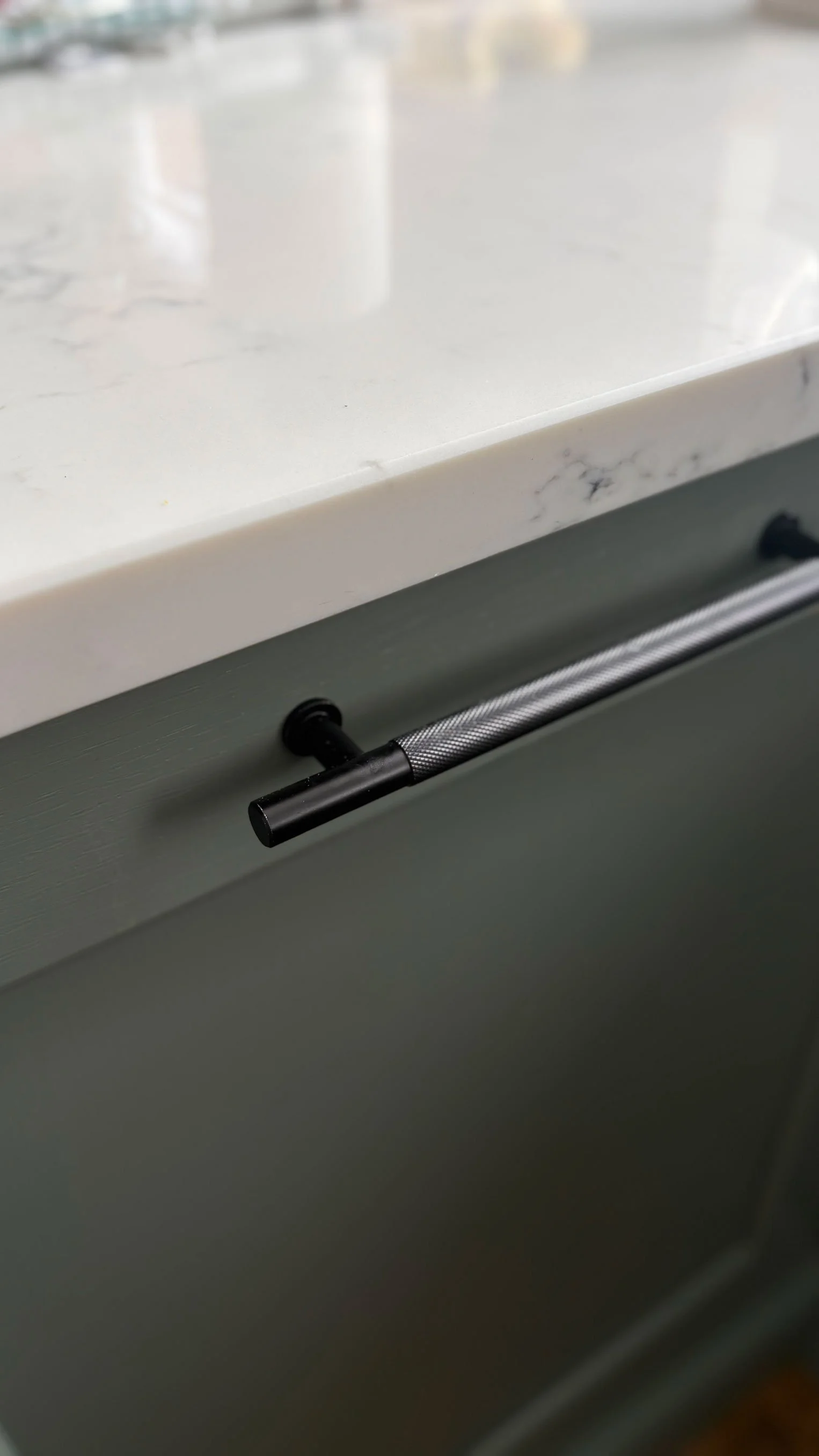 Close-up of a marble countertop with a black metal handle on a drawer beneath it.