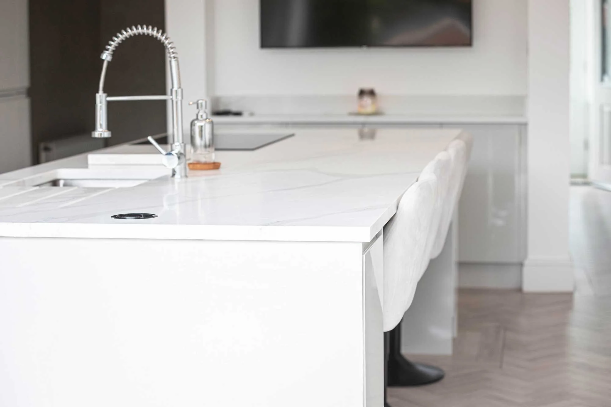 Close-up of a modern white kitchen island with a marble-effect quartz worktop, a chrome spring-neck tap, and a pop-up electrical socket.