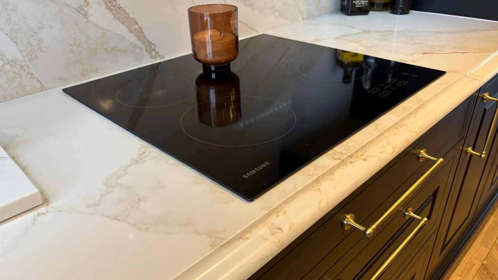 A kitchen countertop with a glass vase holding purple tulips, three gray canisters labeled tea, coffee, and sugar, and part of a white stove with a drawer and round knob.
