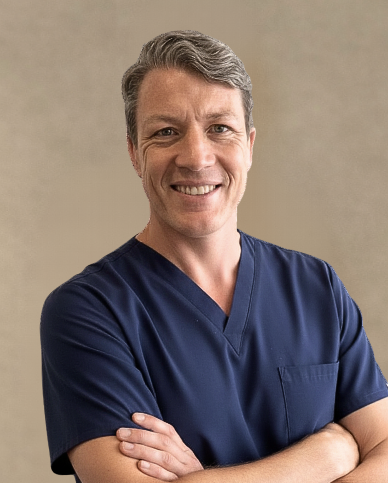 A smiling male healthcare professional wearing navy scrubs, standing with arms crossed against a beige background.