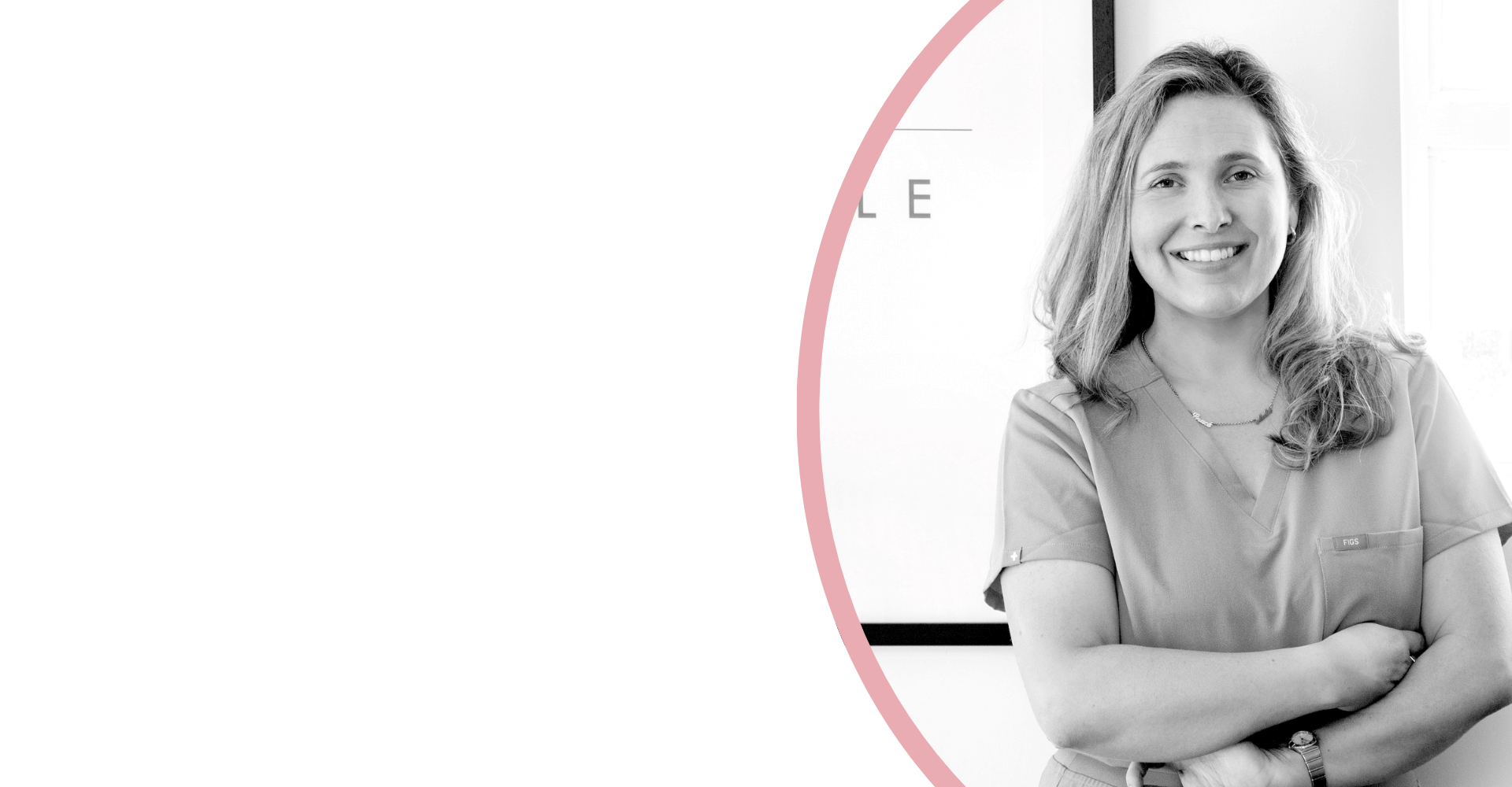 A smiling woman wearing medical scrubs with her arms crossed in a professional setting, black and white photo.