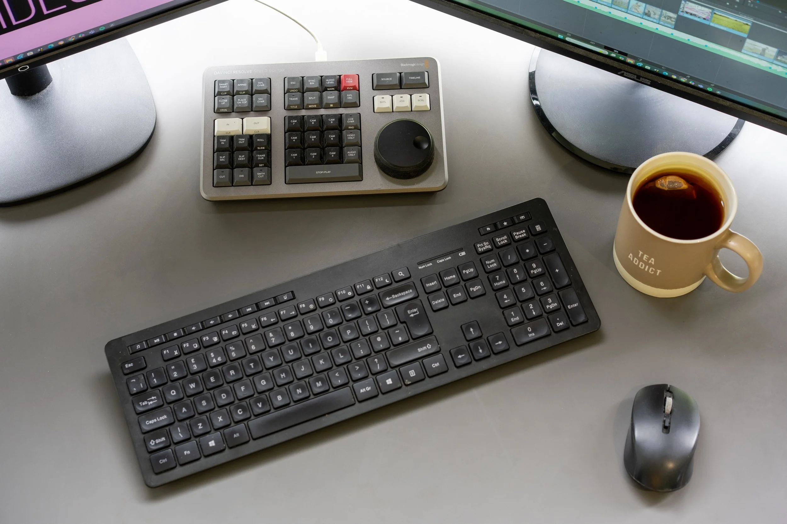 Desk setup with two monitors, a control panel, a keyboard, a computer mouse, and a cup of coffee.