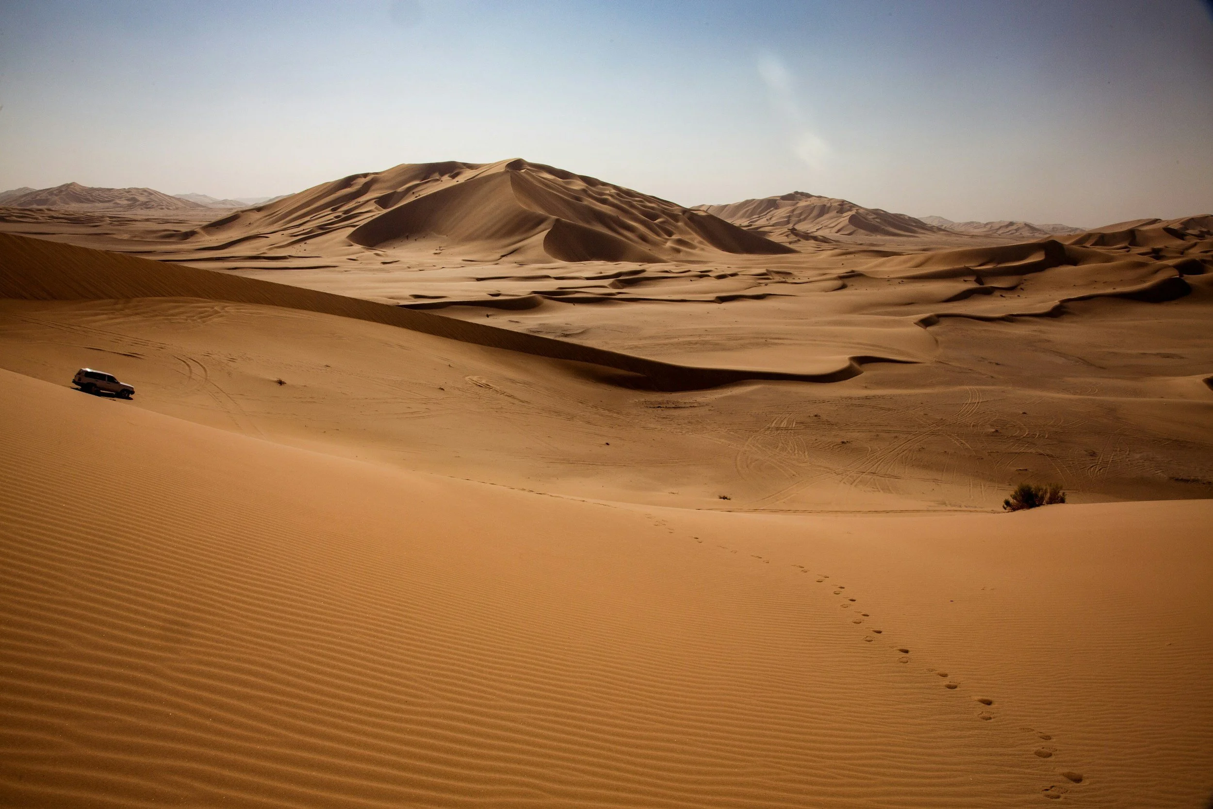 Deserto di dune di sabbia con alcune tracce di passaggi di veicoli e un'auto in lontananza.