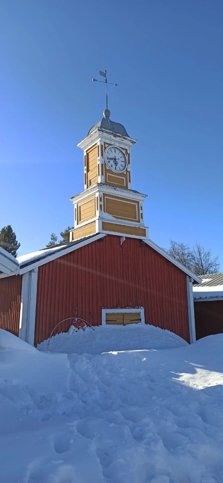 Una torre con orologio e tempo, sopra un edificio rosso, con neve e cielo blu