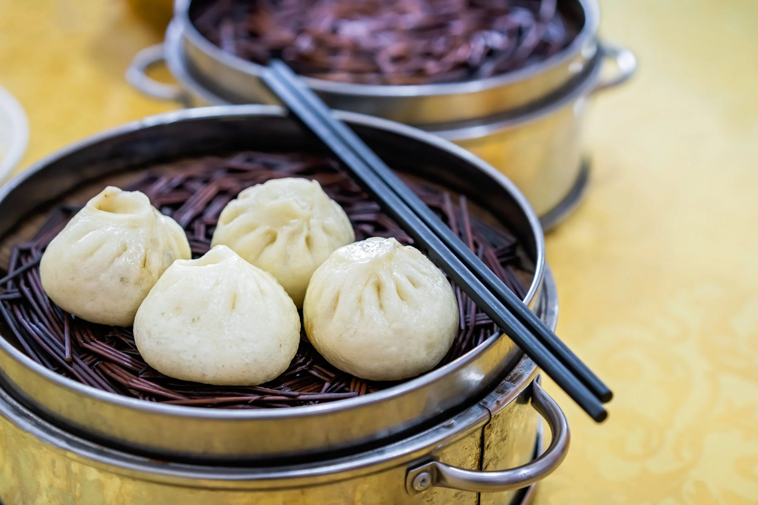 Cinque dumplings su un cestino di vimini, con due scatole di ingredienti o condimenti sullo sfondo.