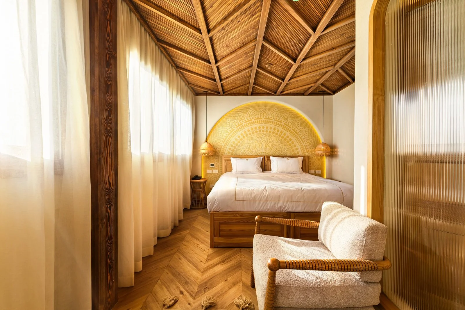 Camera da letto moderna con pareti chiare, letto con testiera ricamata, armadio in legno, illuminazione calda, e divano beige in primo piano.