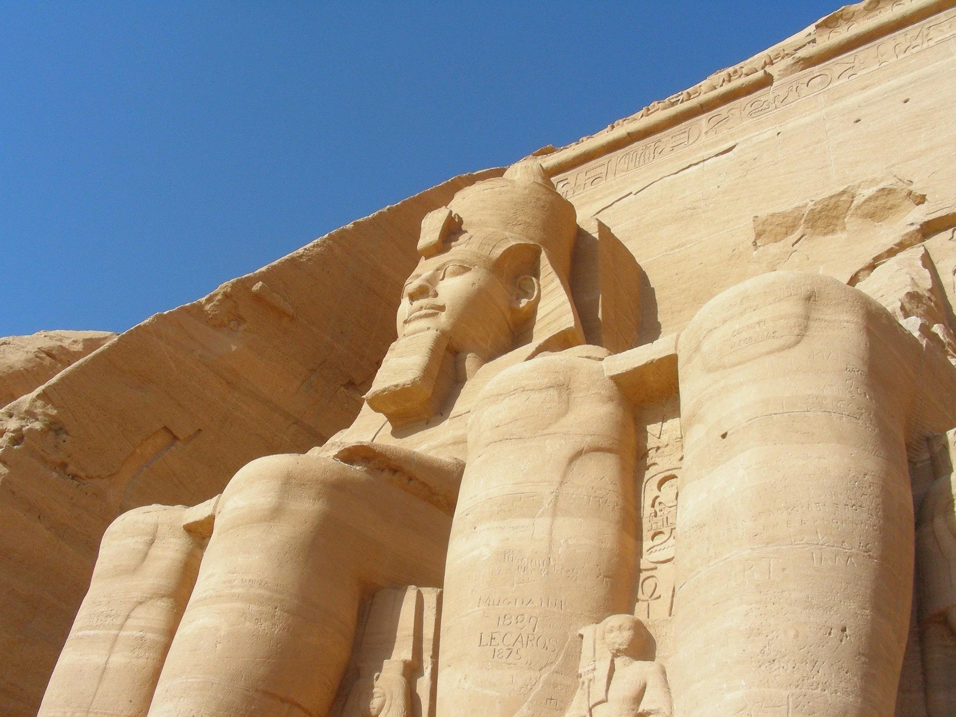 Statua di un faraone egizio scolpita in pietra, probabilmente a Karnak, con geroglifici sullo sfondo, sotto un cielo blu