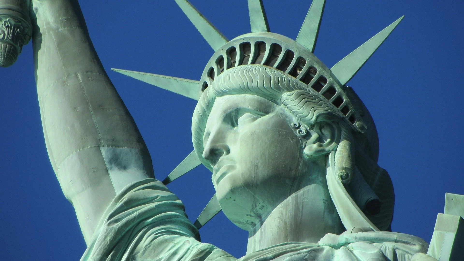 Dettaglio della Statua della Libertà, in primo piano il volto e la corona con le punte, con uno sfondo di cielo blu.