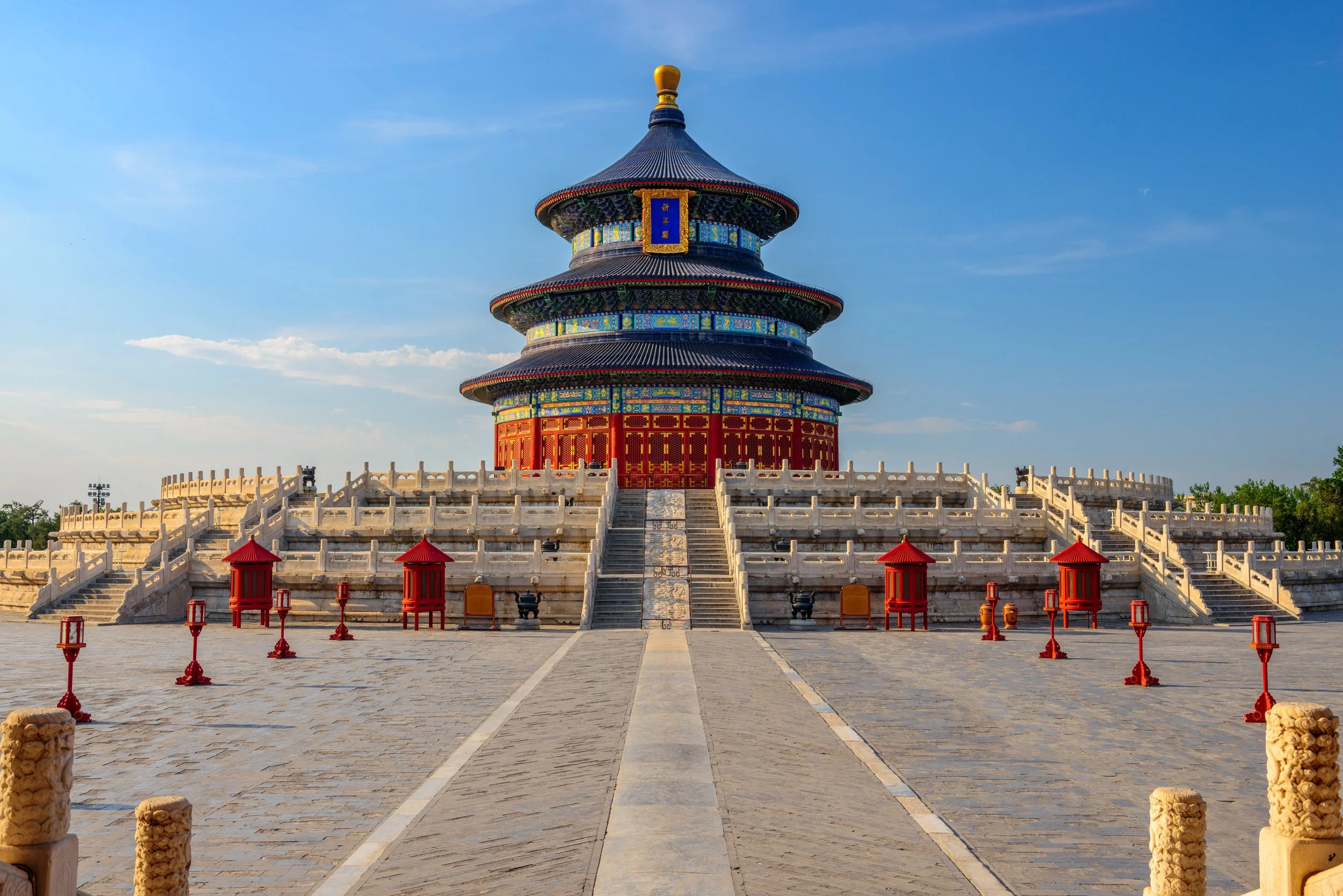 Templo cinese con tetto a pagoda, decorazioni colorate, accesso con scale di pietra, circondato da lanterne rosse e un cortile di pietra.
