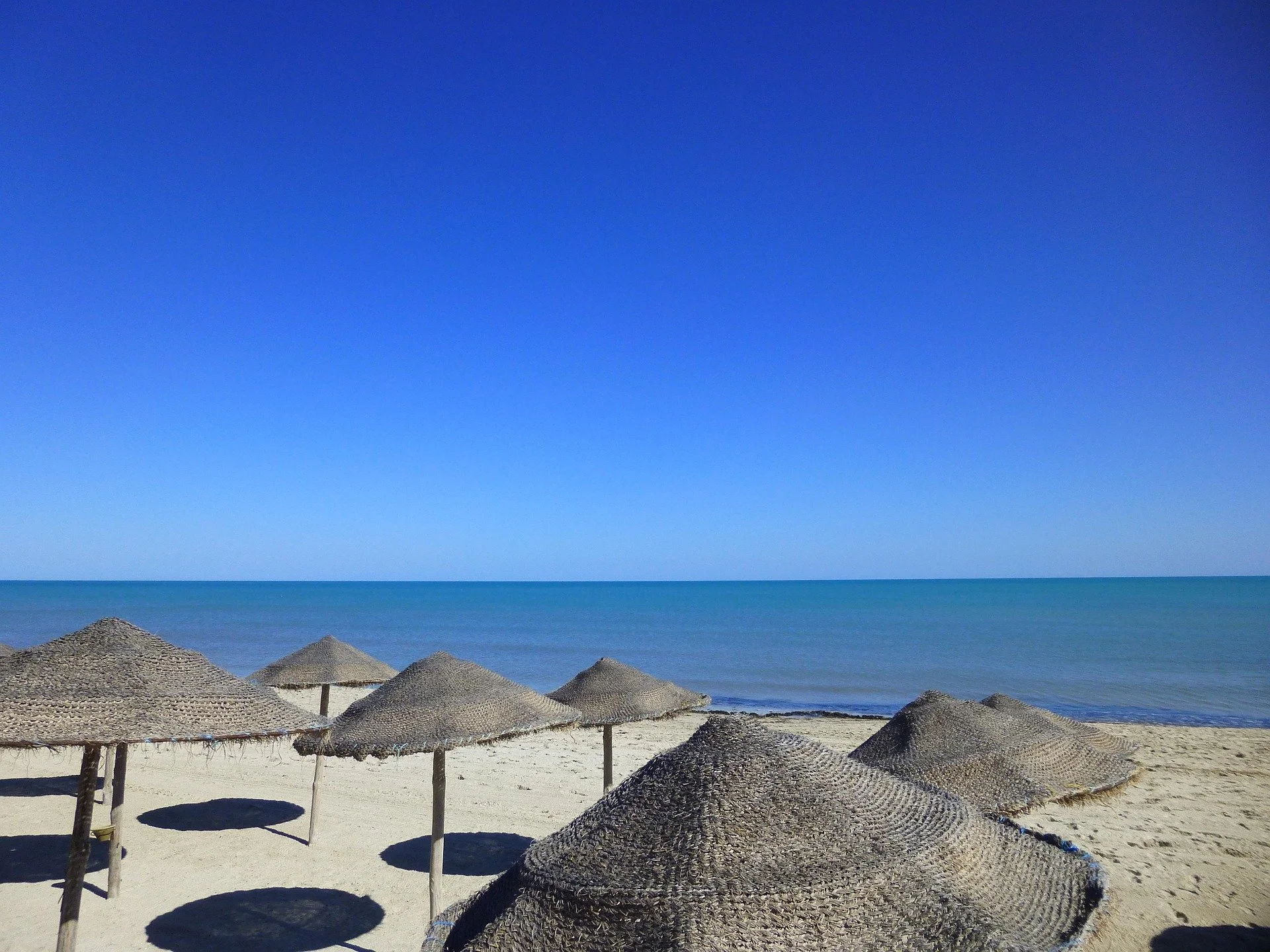 Tavolozza di ombrelloni e pagode di paglia sulla spiaggia con il mare e il cielo azzurro in stile vacanza