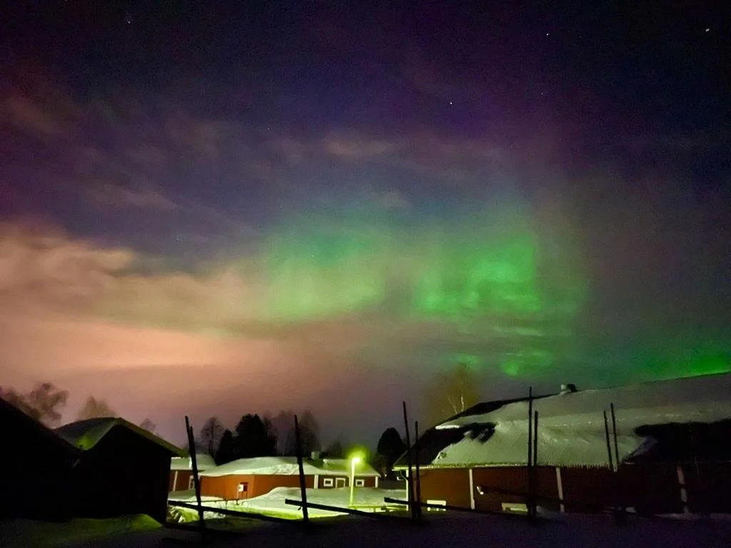 Aurora boreale verde nel cielo notturno sopra case con tetto innevato