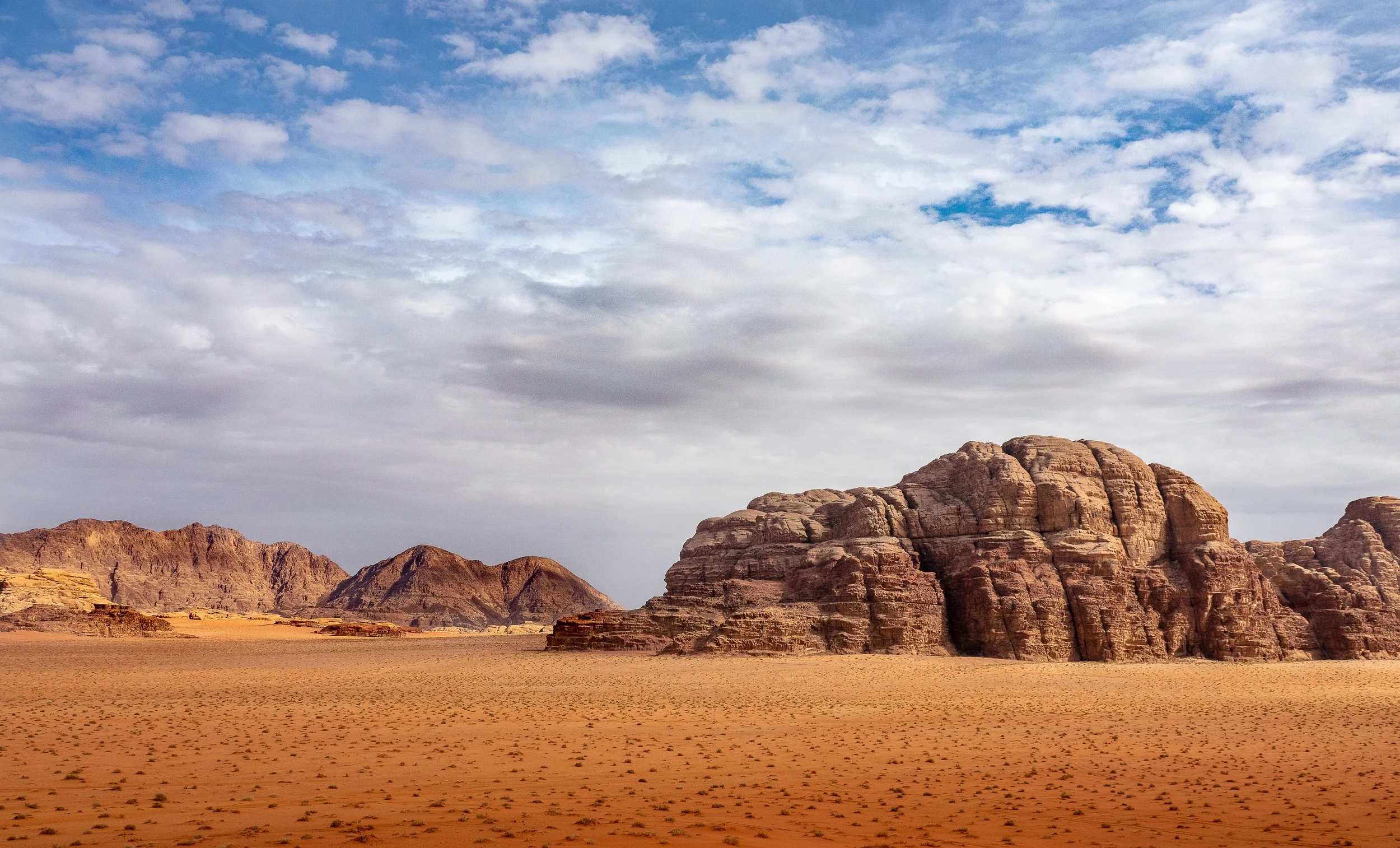 Paesaggio desertico con rocce di colore marrone e un cielo parzialmente nuvoloso.