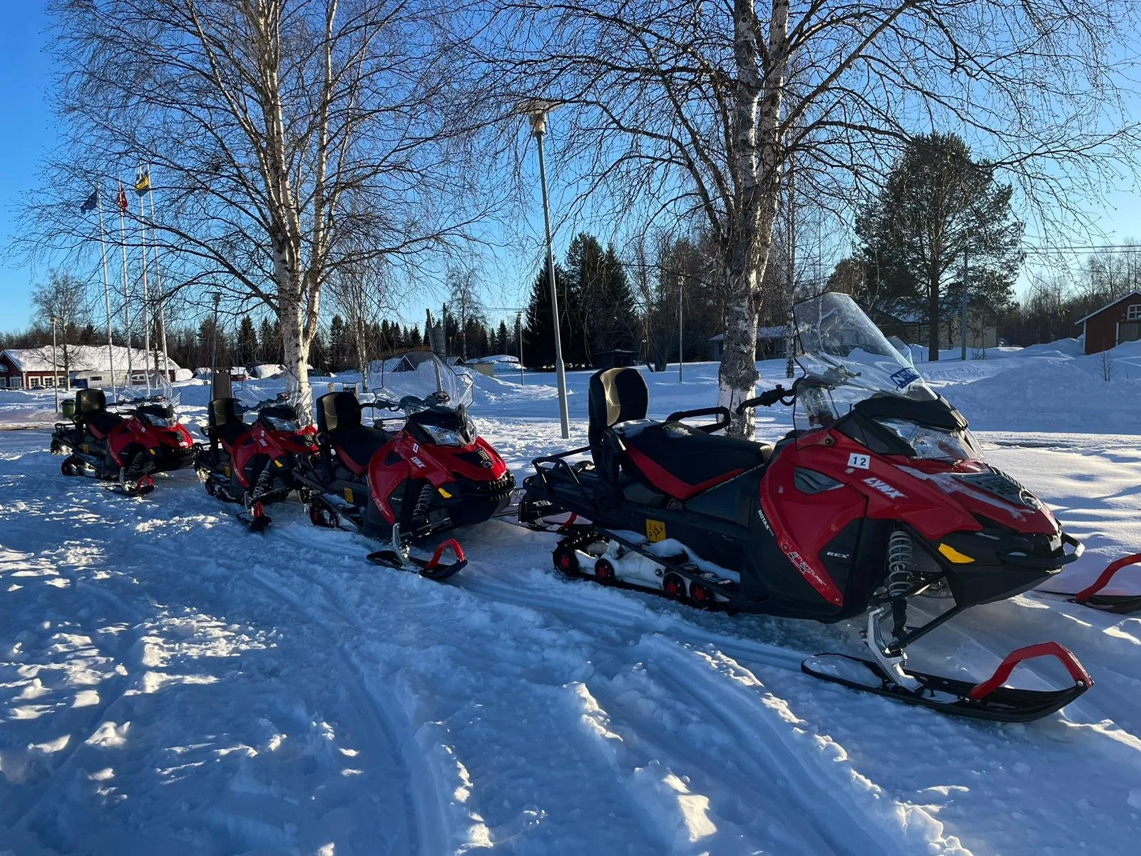 Cinque motoslitte rosse parcheggiate sulla neve con alberi e case in uno scenario invernale