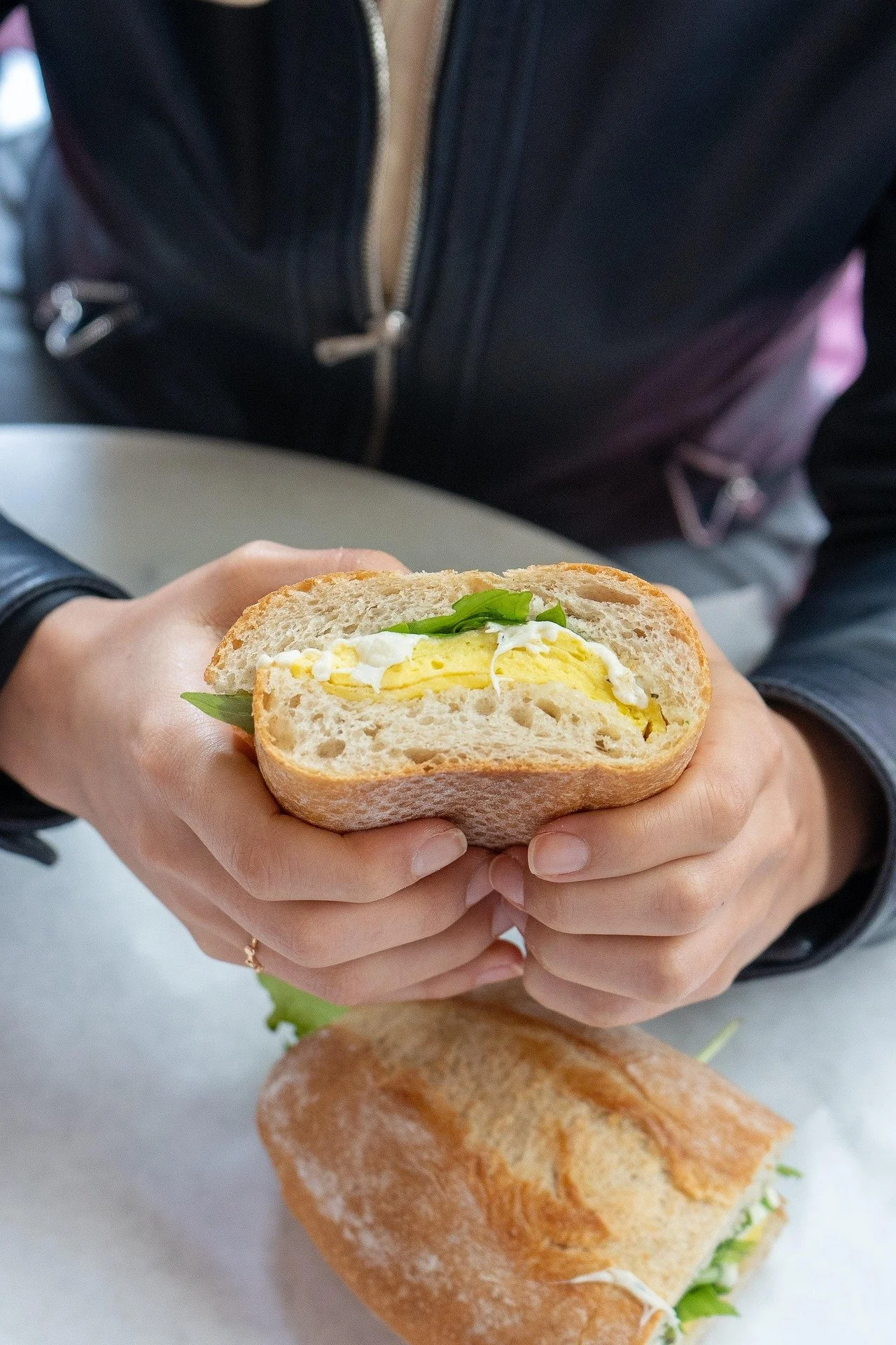 Una persona tiene in mano un panino con uova e erba cipollina, sul tavolo si vede altro pane e un altro panino.