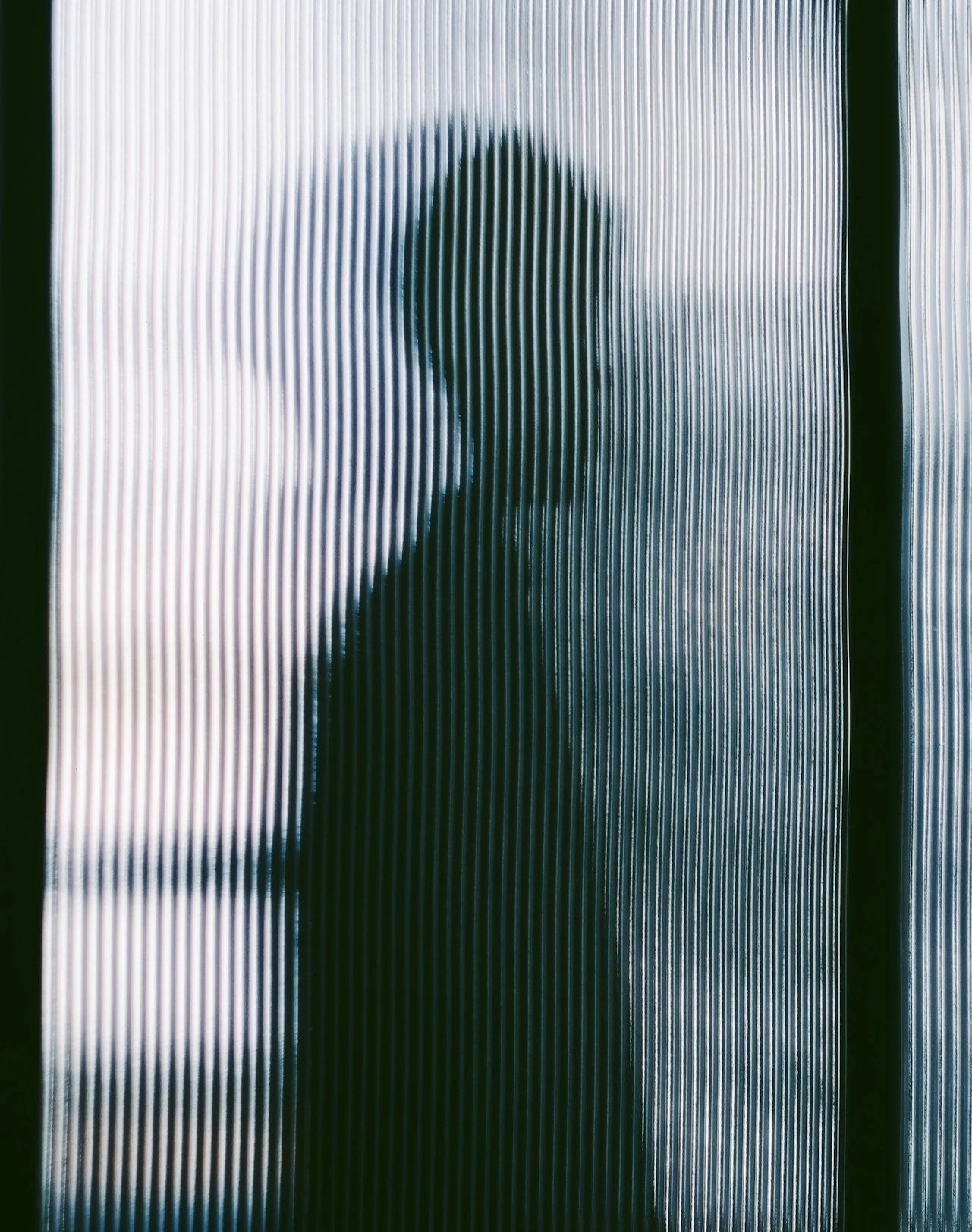 Silhouette of a person's profile seen through textured, ribbed glass or plastic.