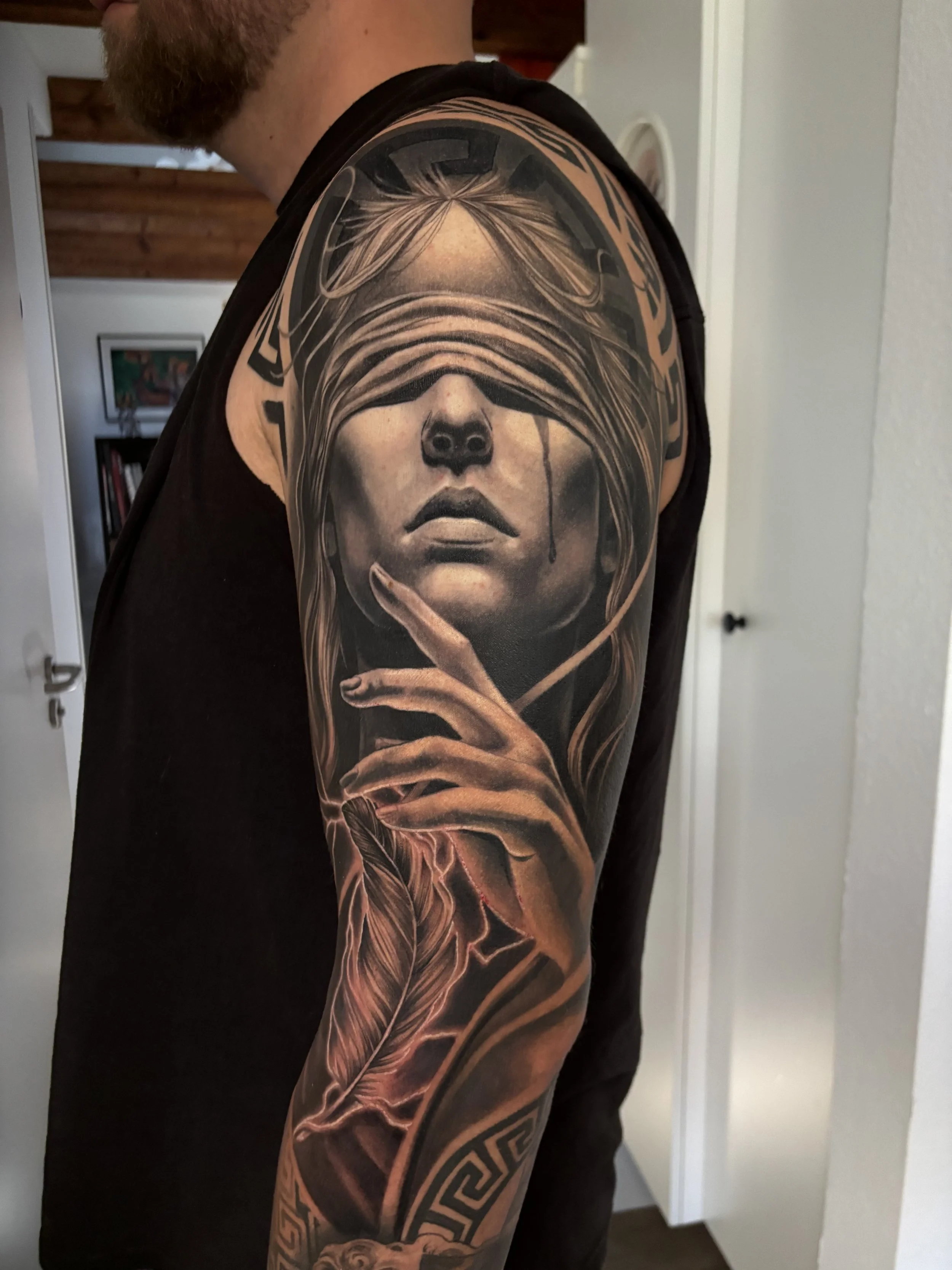 Tattoo of a woman with a blindfold over her eyes, holding a finger to her lips, on a man's upper arm.